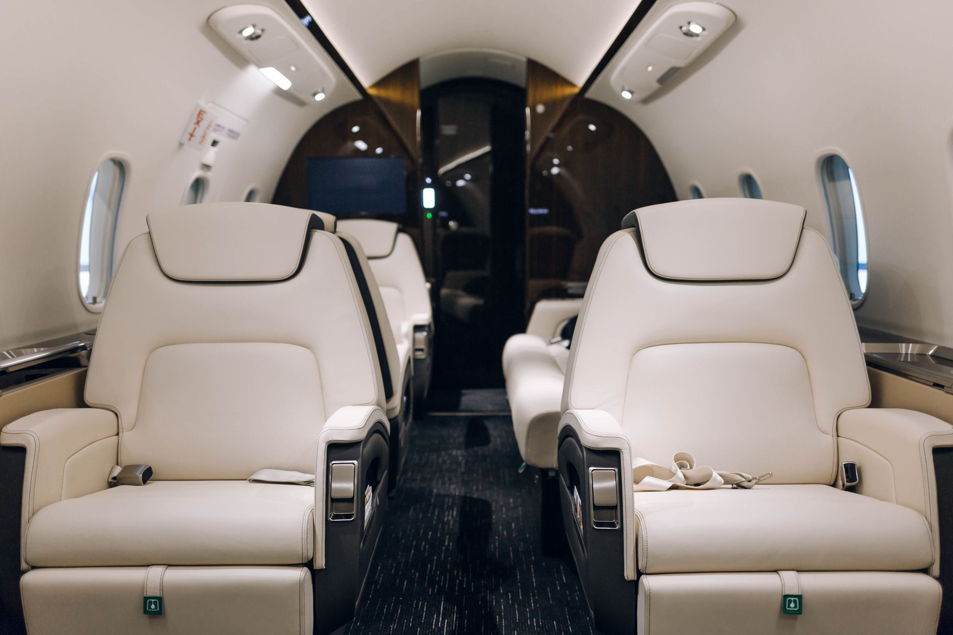 Luxurious interior of a private jet with cream leather seats arranged in pairs facing each other over a dark carpet.