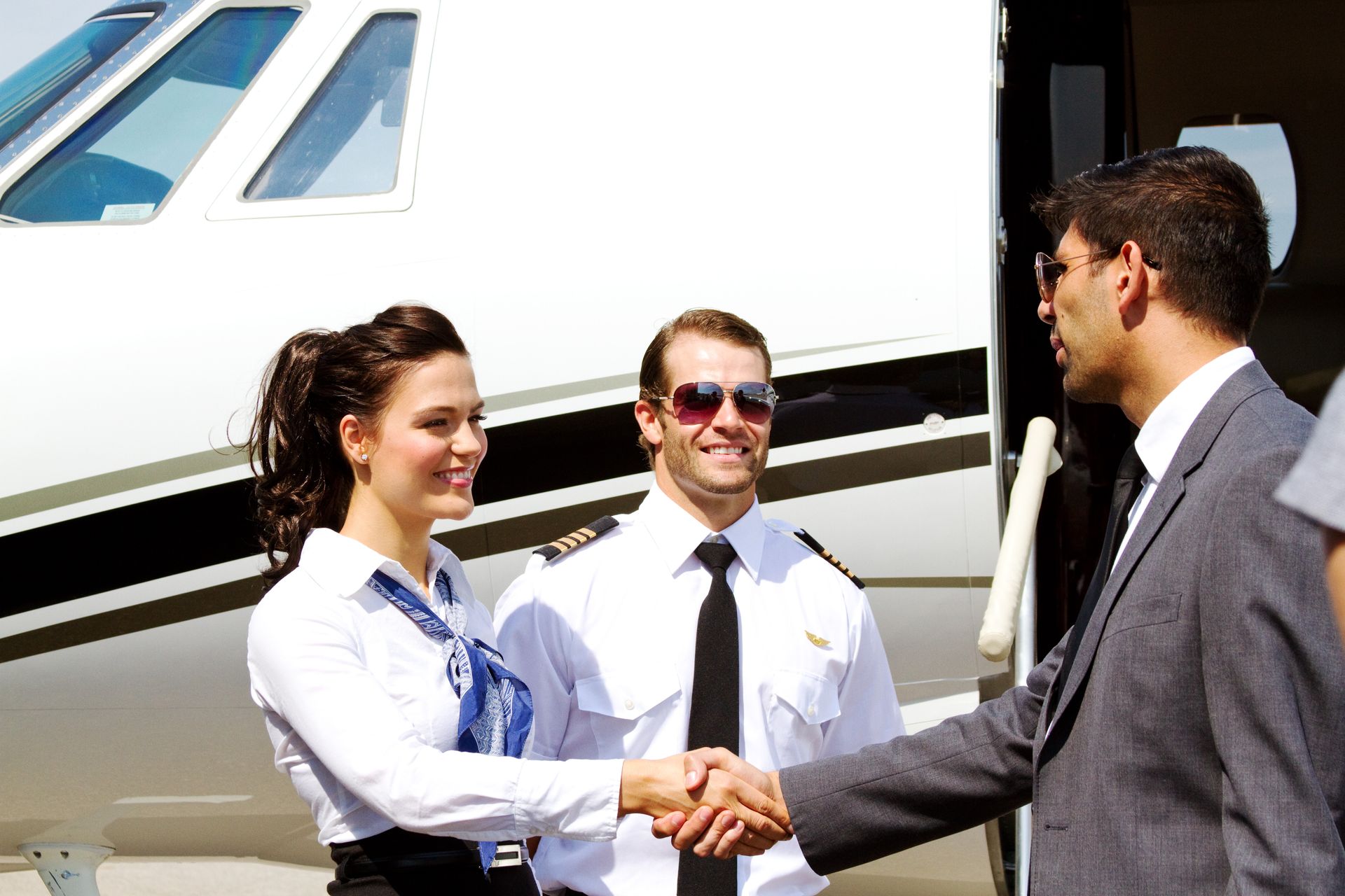 A flight crew member and a pilot in uniform shake hands with a person in a suit in front of a private jet.