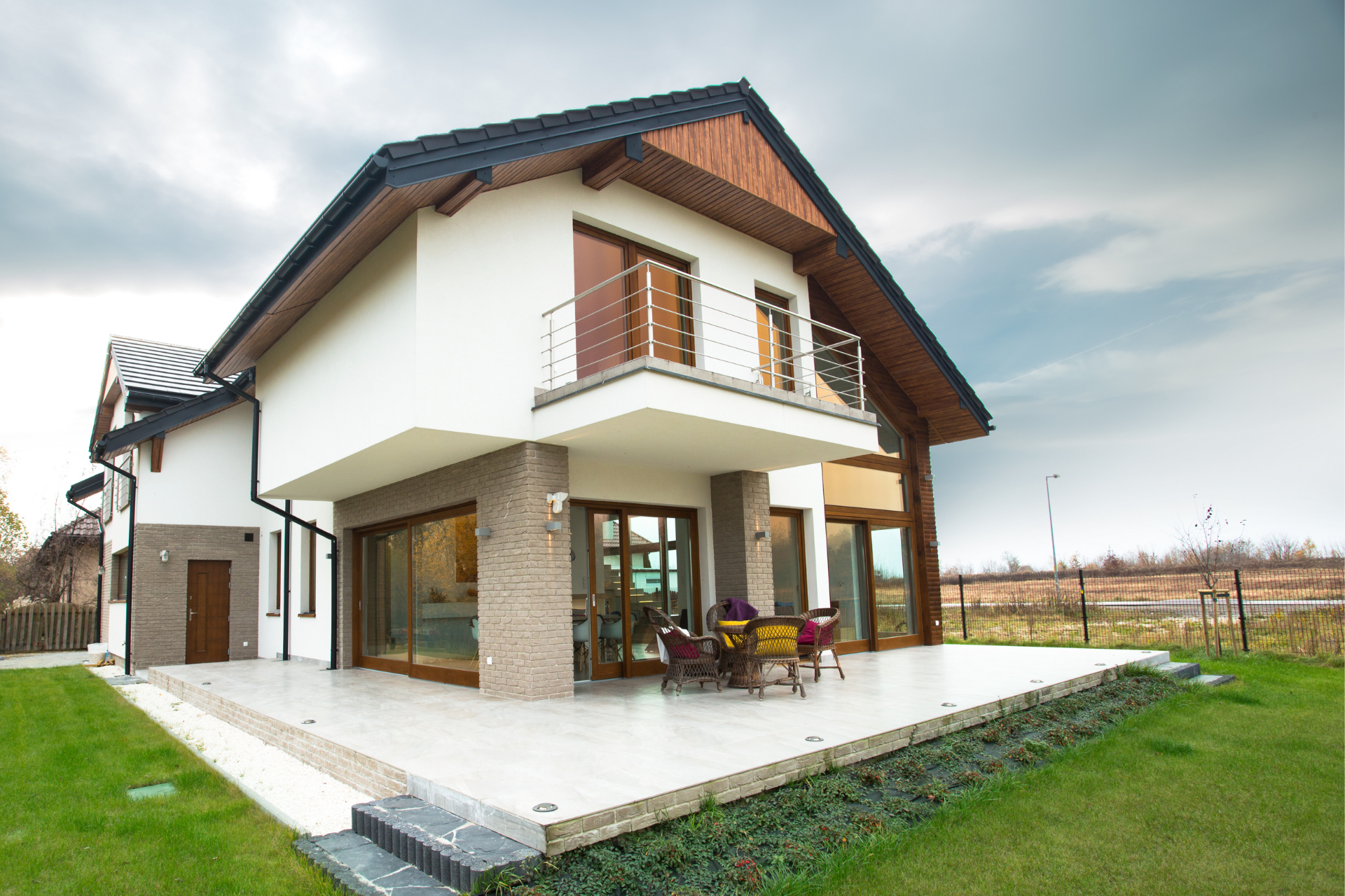 A large white custom home with a balcony and a large lawn in front of it.