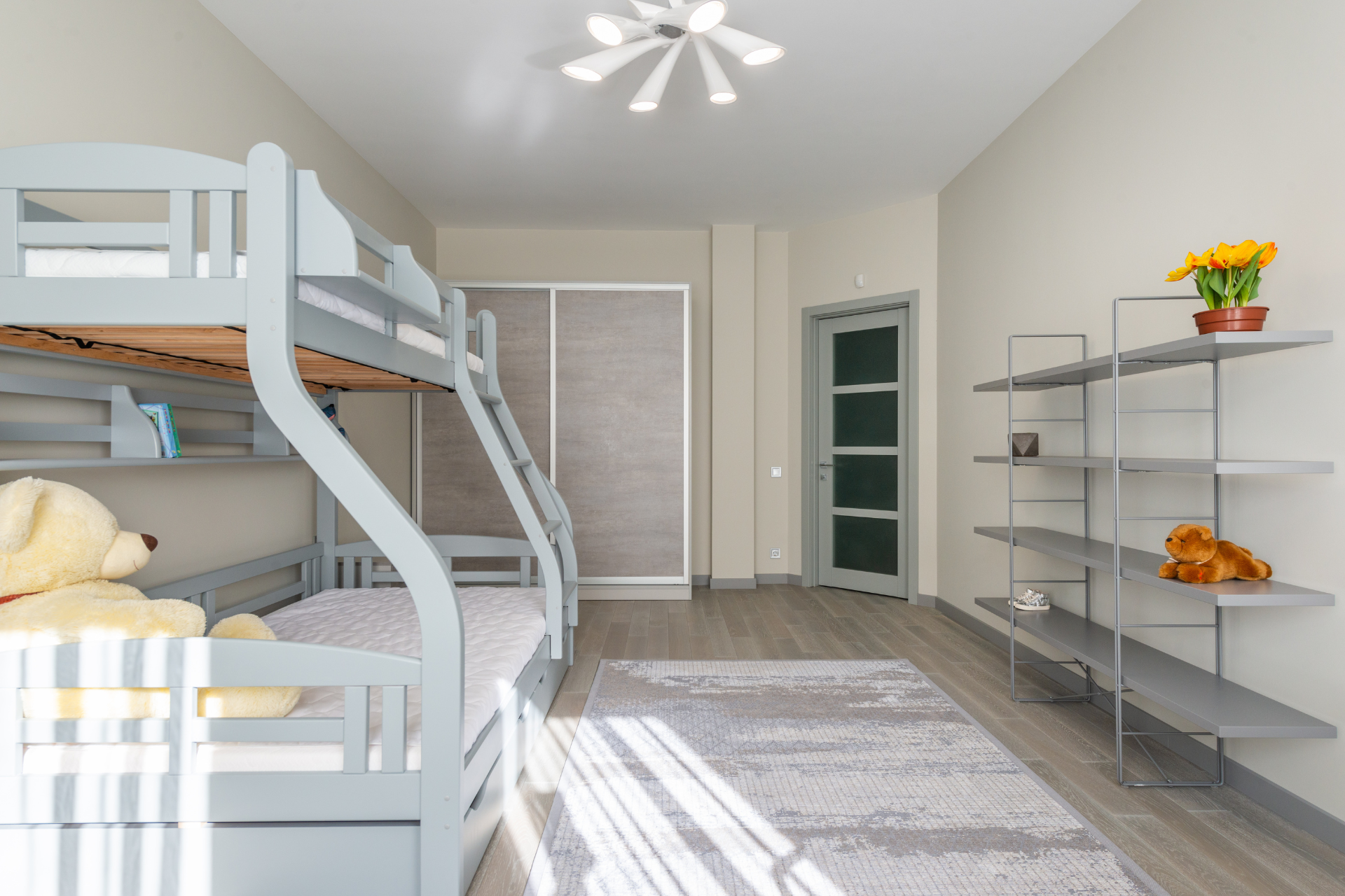 A bedroom with bunk beds, shelves, a rug and a teddy bear.