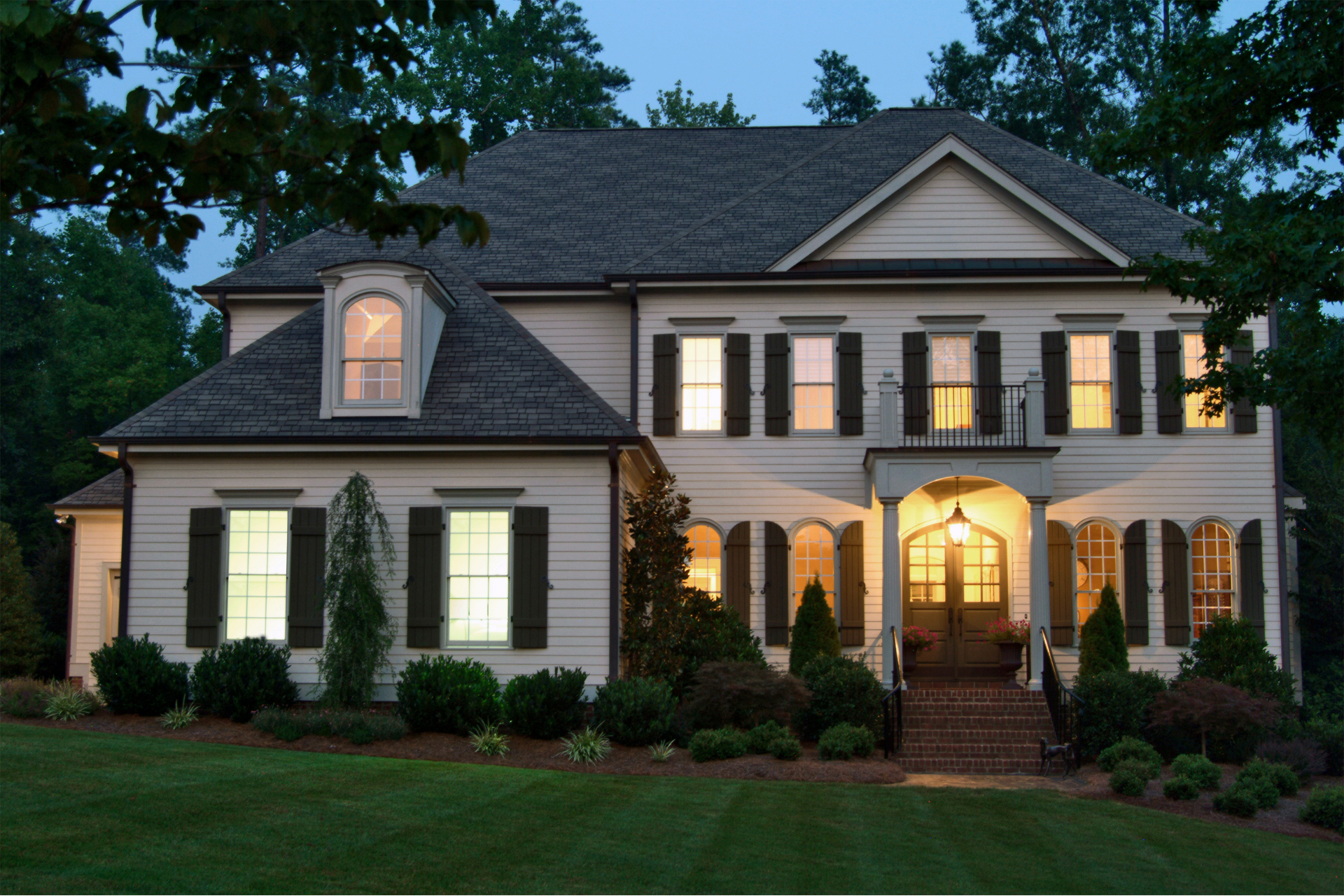 A large white custom home with black shutters is lit up at night