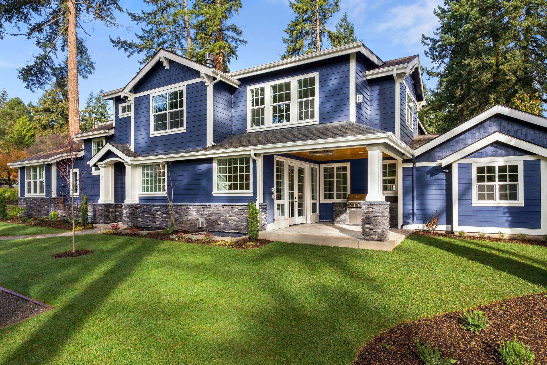 A large blue custom home with a lush green lawn in front of it.