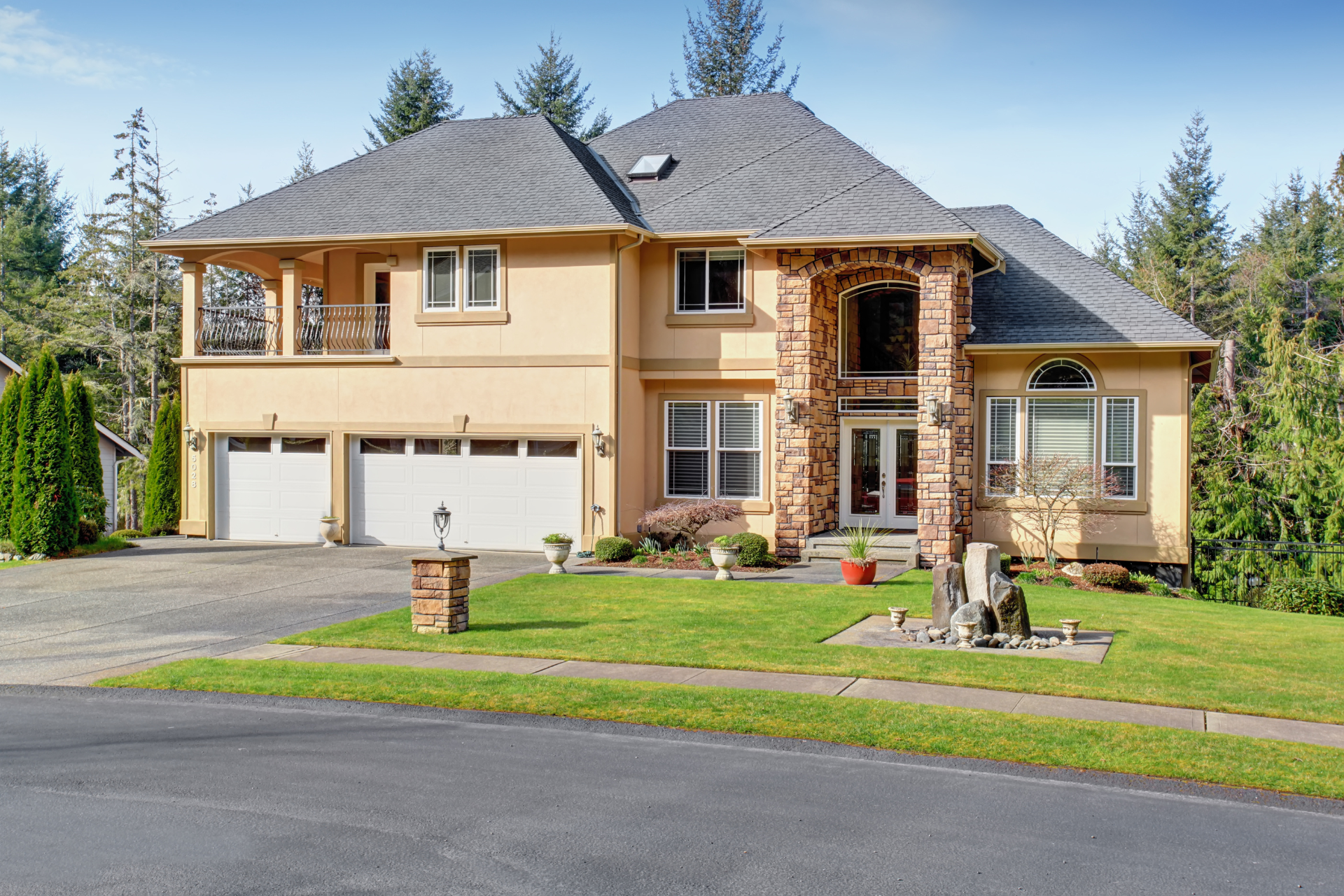A large custom home with a gray roof is sitting on top of a lush green hillside.