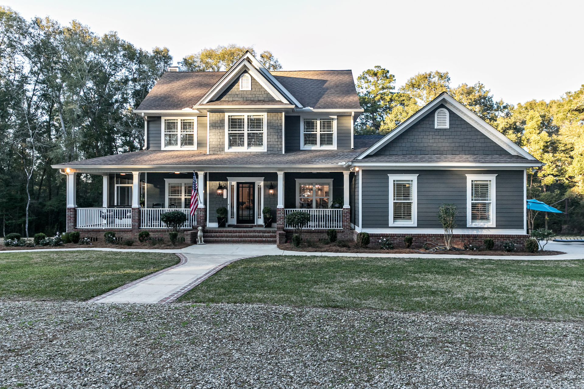 A large gray custom home with a large porch is sitting on top of a lush green field.