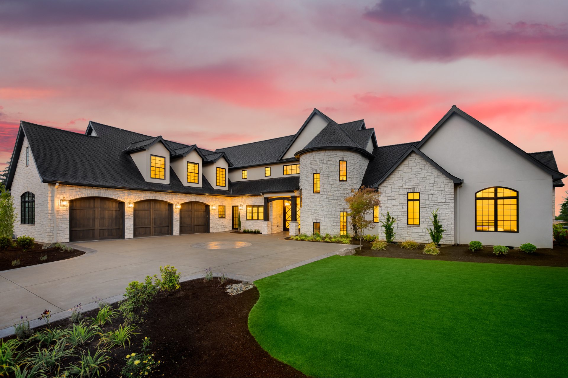 A large white custom home with a black roof is sitting on top of a lush green lawn.