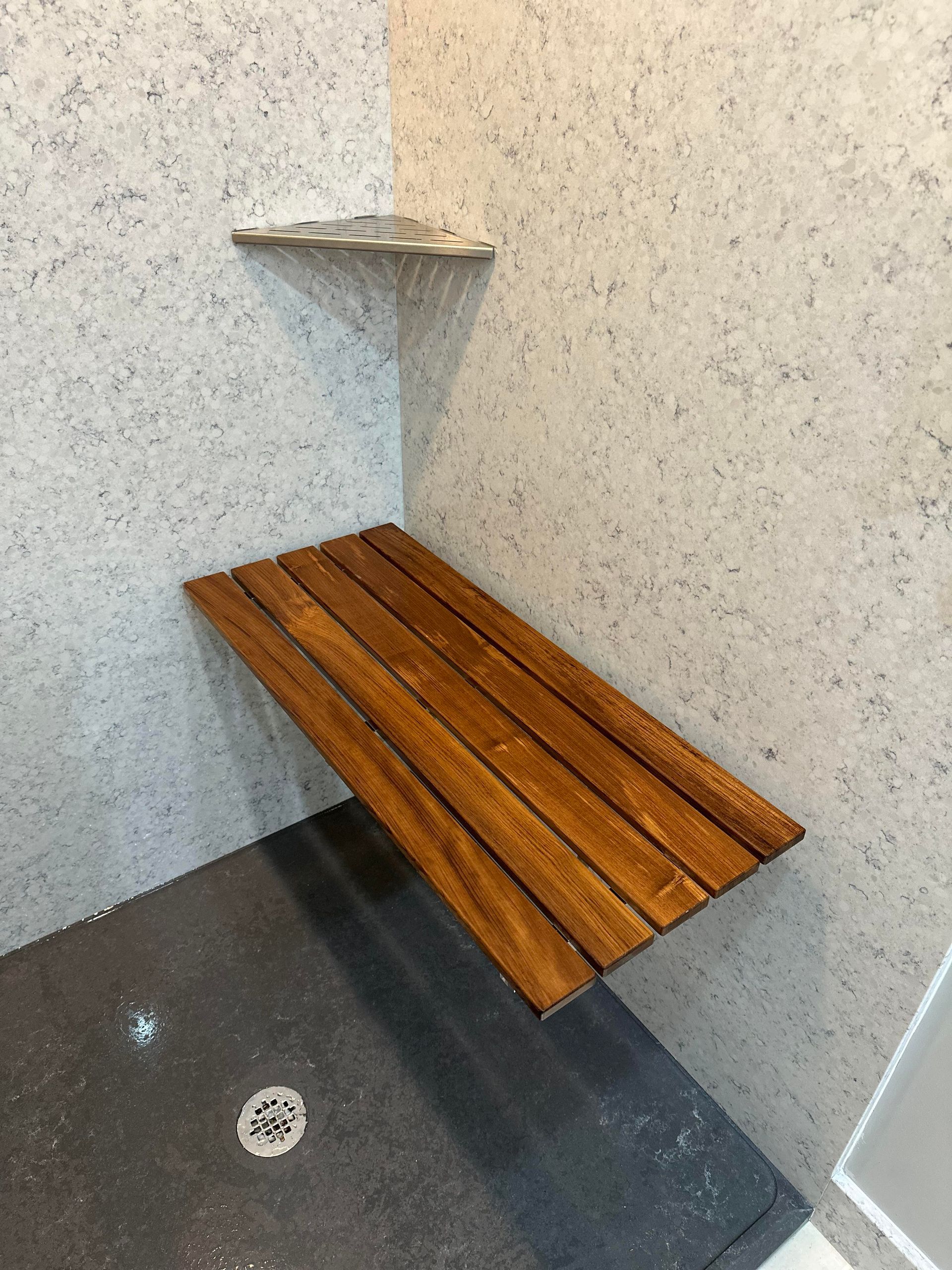 A shower with a wooden bench and a shelf on the wall.