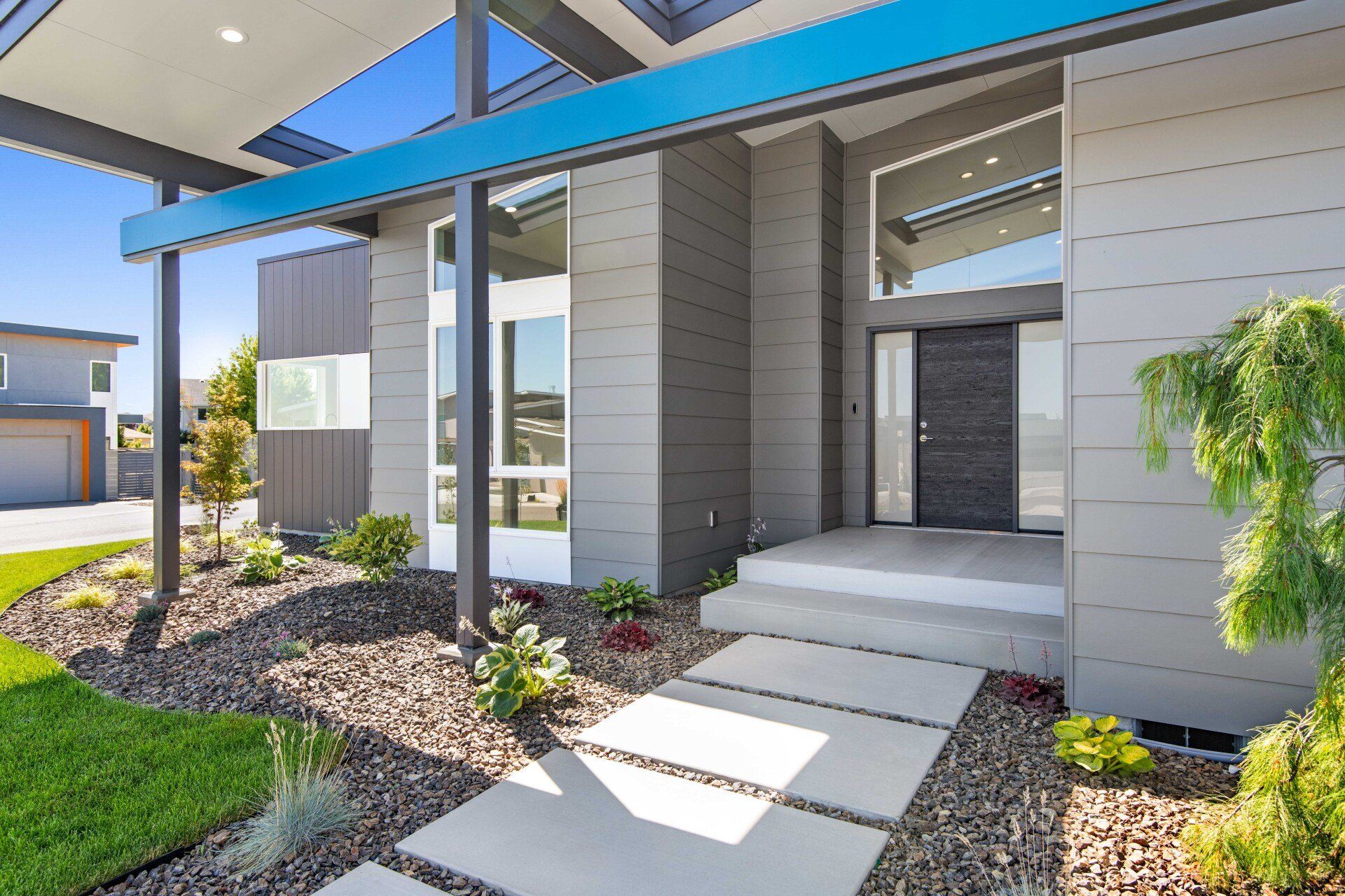 A modern house with a blue roof and a walkway leading to the front door.