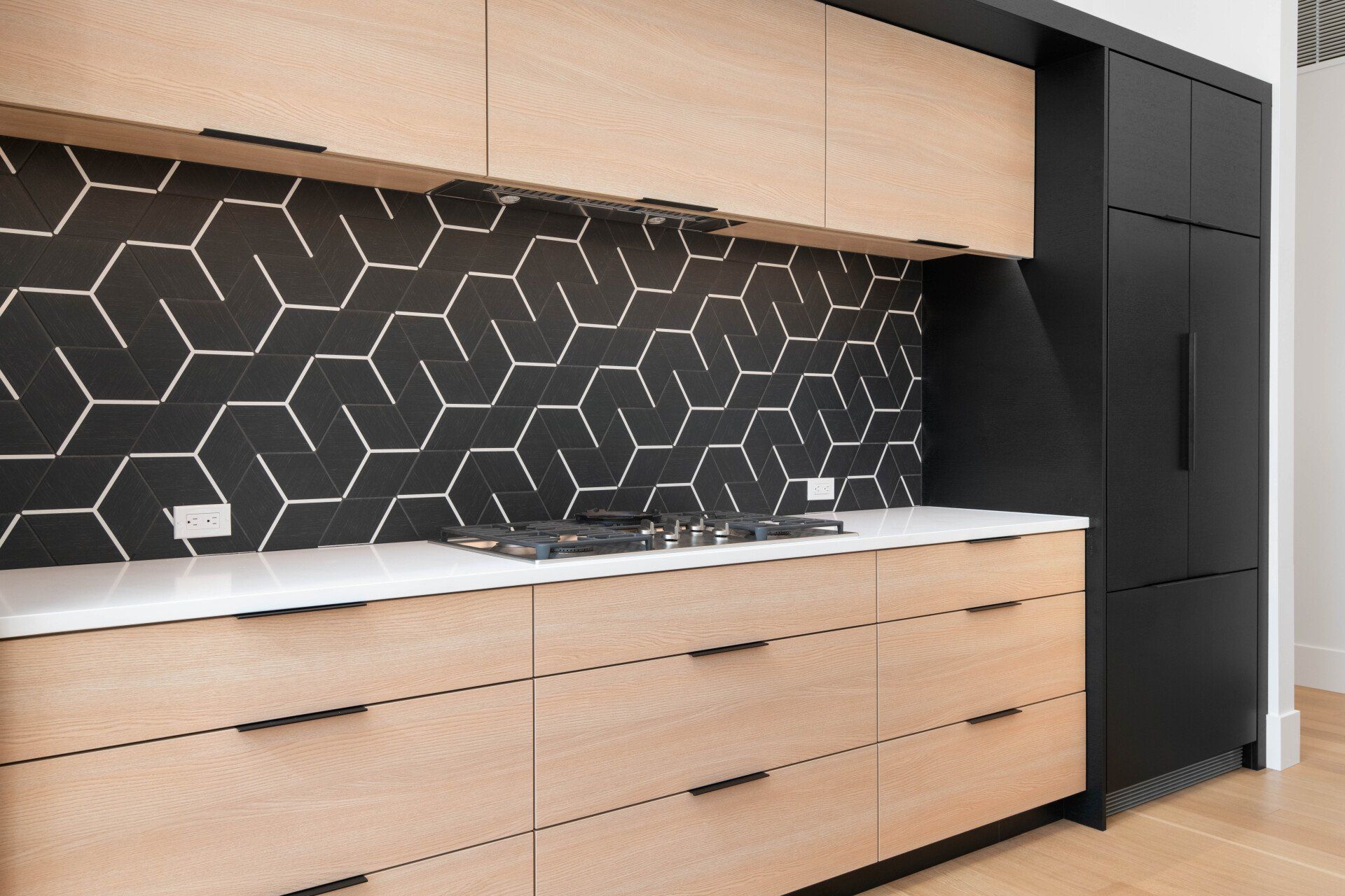 A kitchen with wooden cabinets and black tiles on the wall.
