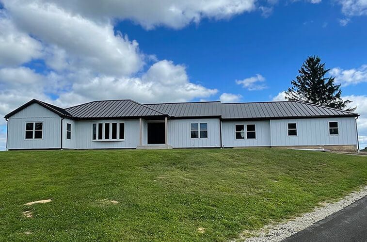 A large white house with a black roof is sitting on top of a lush green hill.