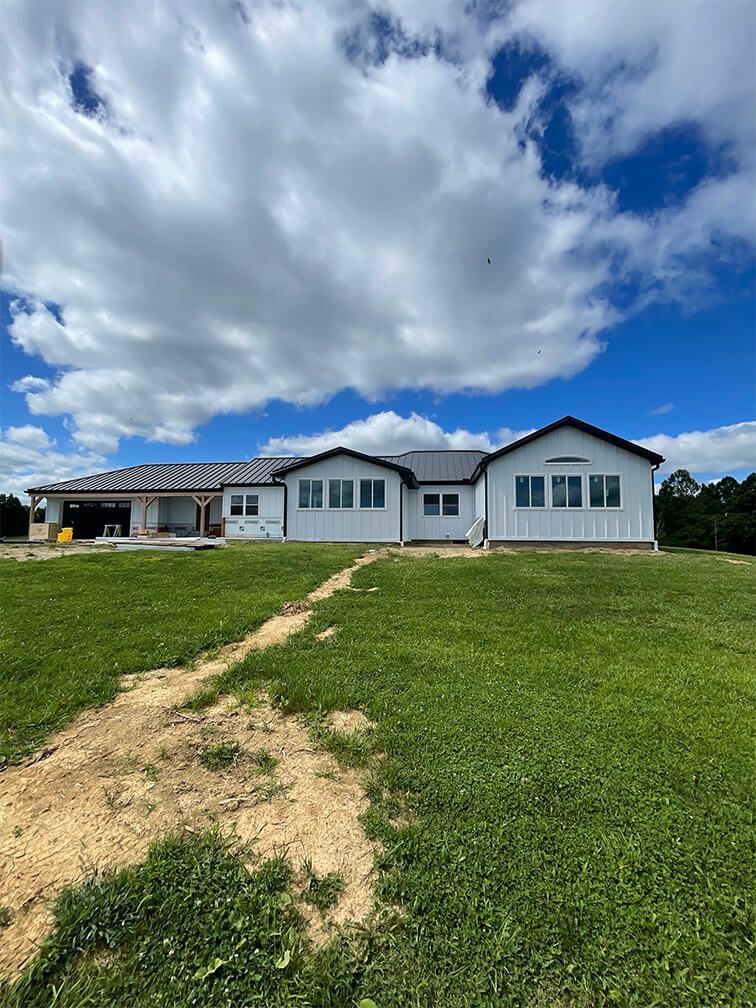 A large white house is sitting on top of a lush green field.