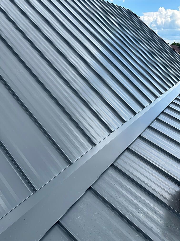A close up of a gray metal roof with a blue sky in the background.
