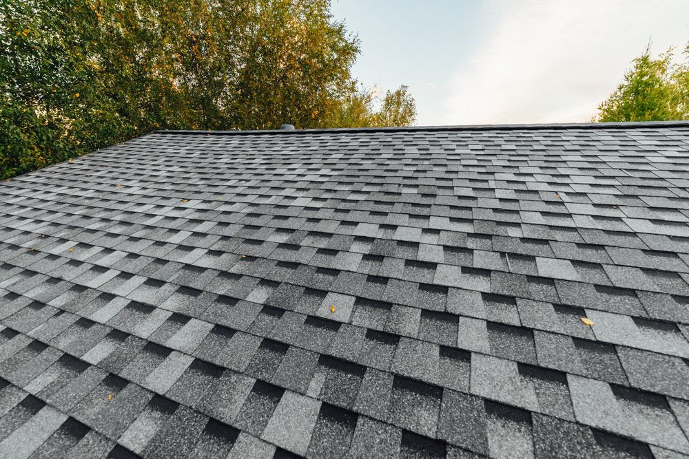 A close up of a roof with a lot of shingles and trees in the background.