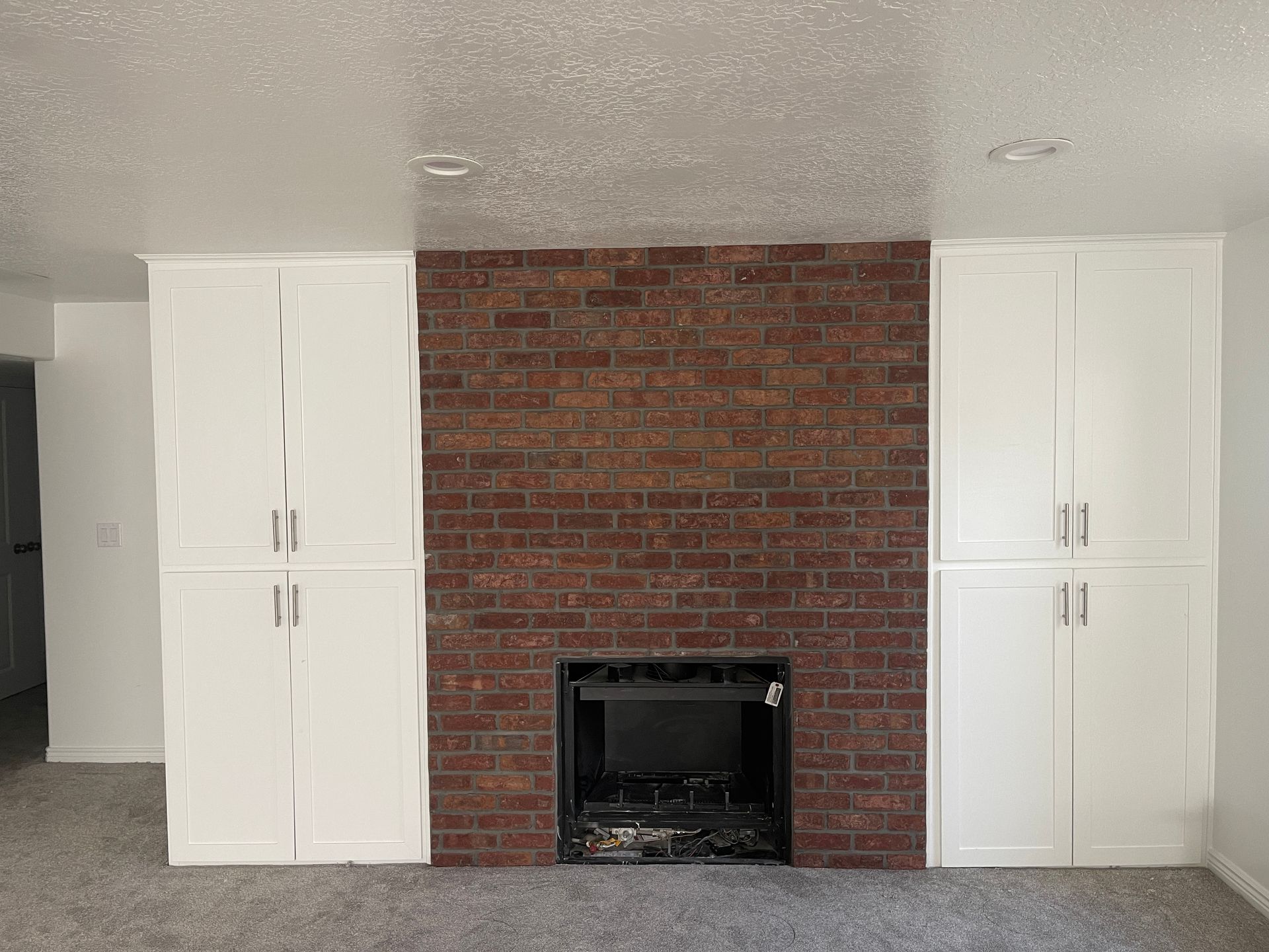 A living room with a brick fireplace and white cabinets.