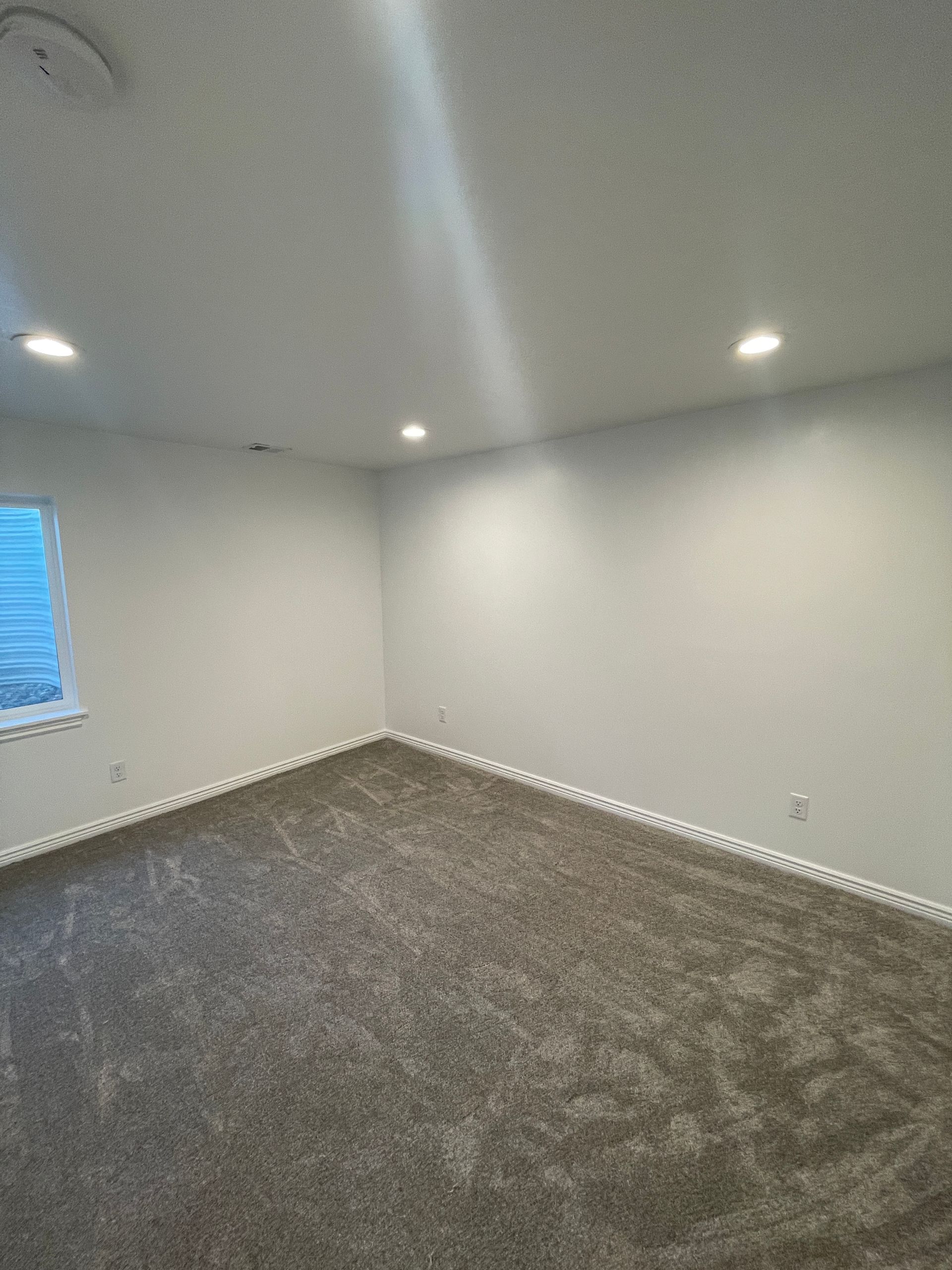 An empty room with a carpeted floor , white walls and a window.