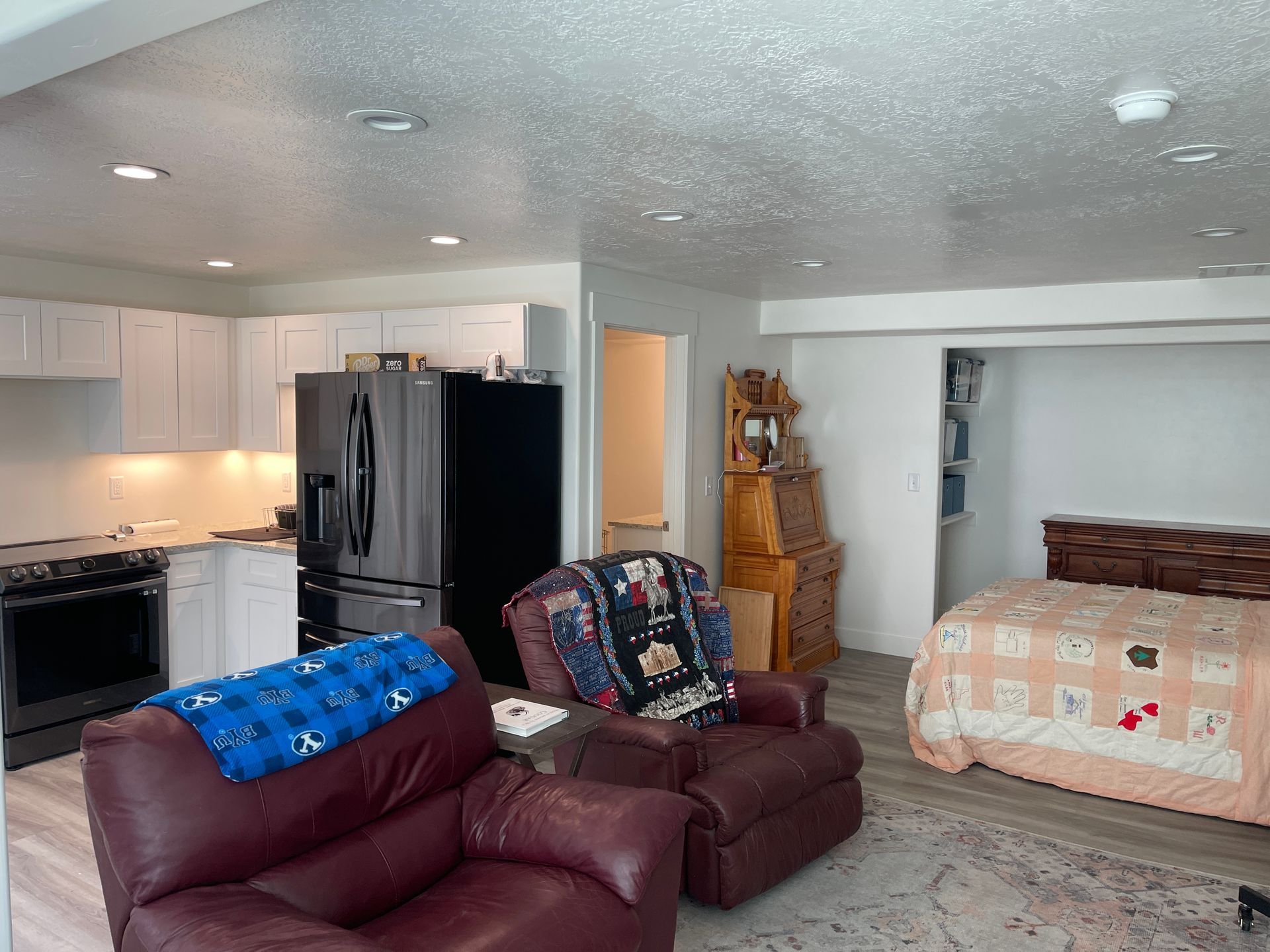 A living room with a couch , chair , refrigerator , and bed.