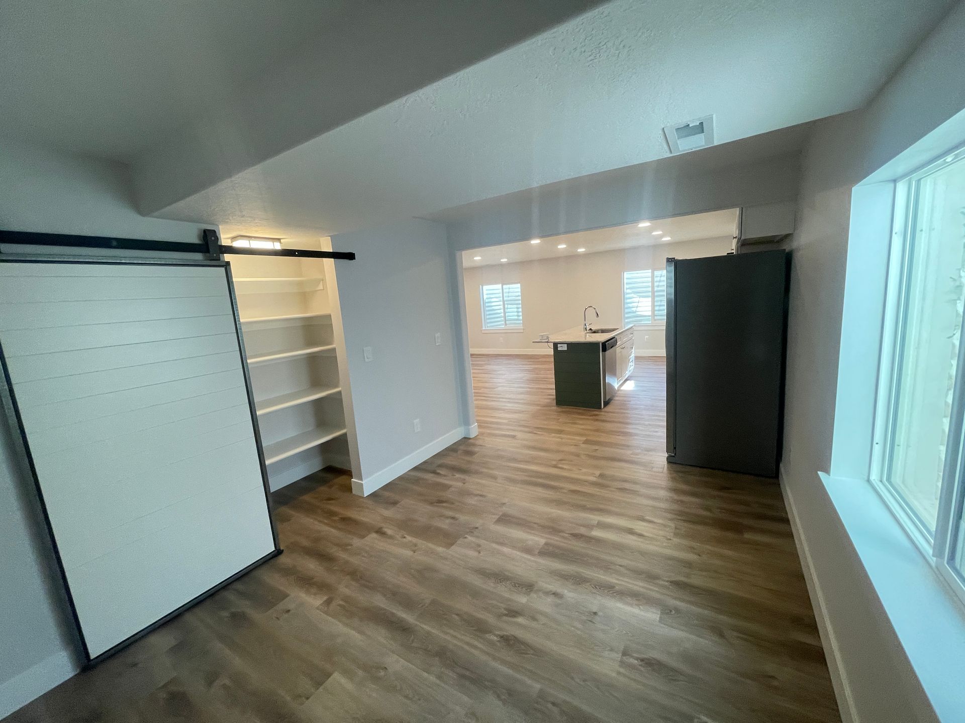 A living room with hardwood floors and a sliding barn door leading to a kitchen.