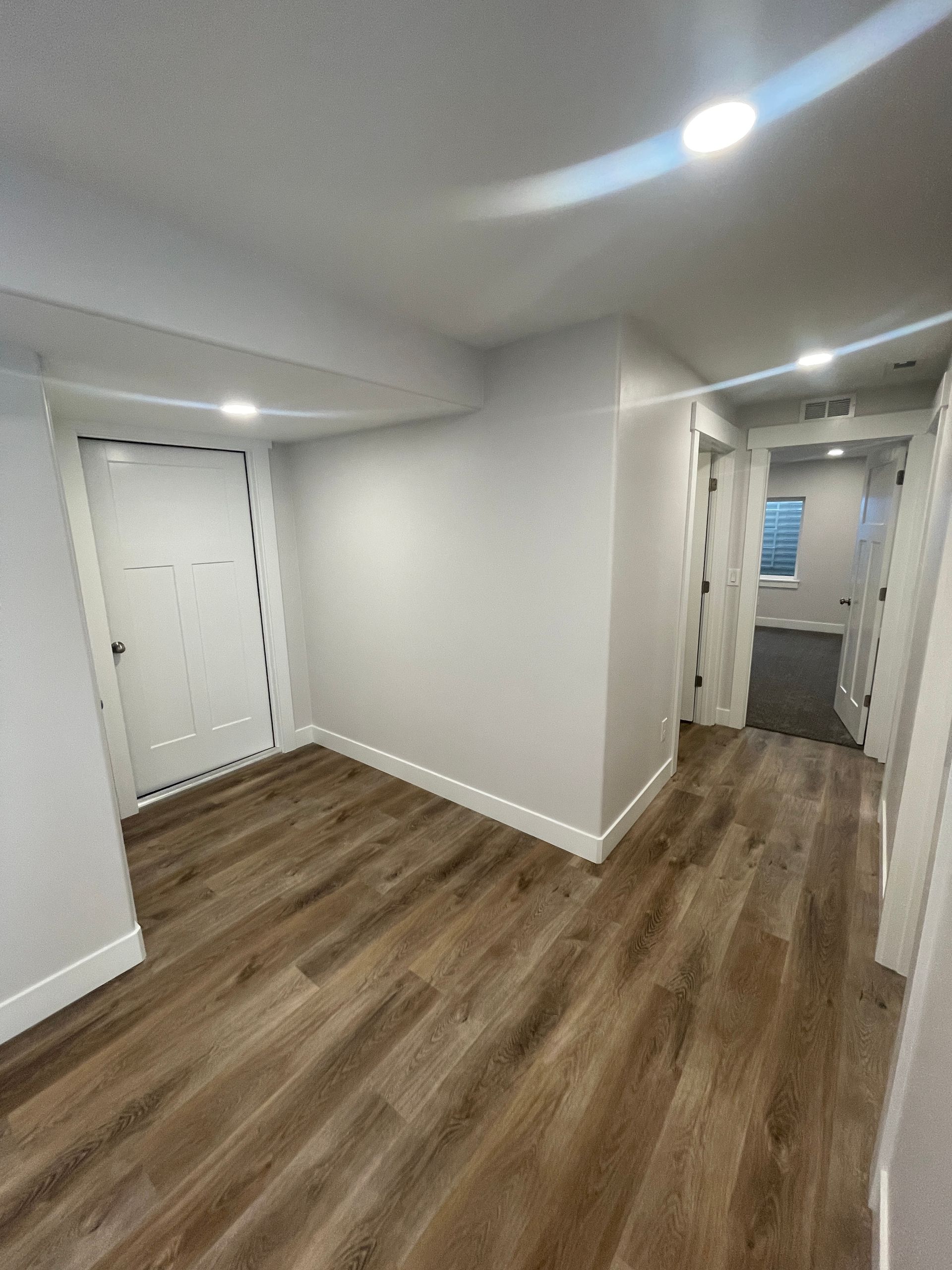 A hallway in a basement with hardwood floors and white walls.