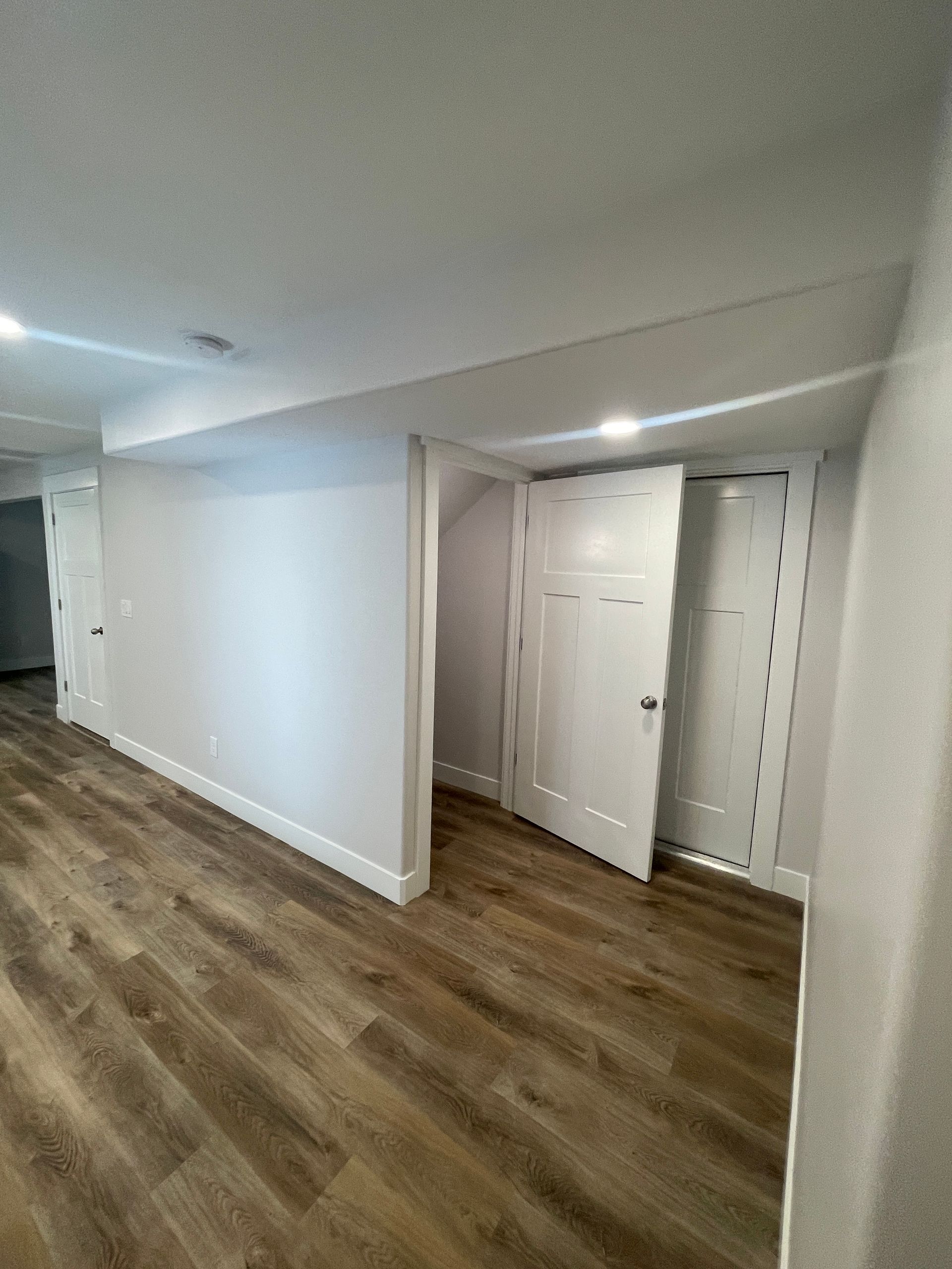 A hallway in a basement with hardwood floors and white walls.