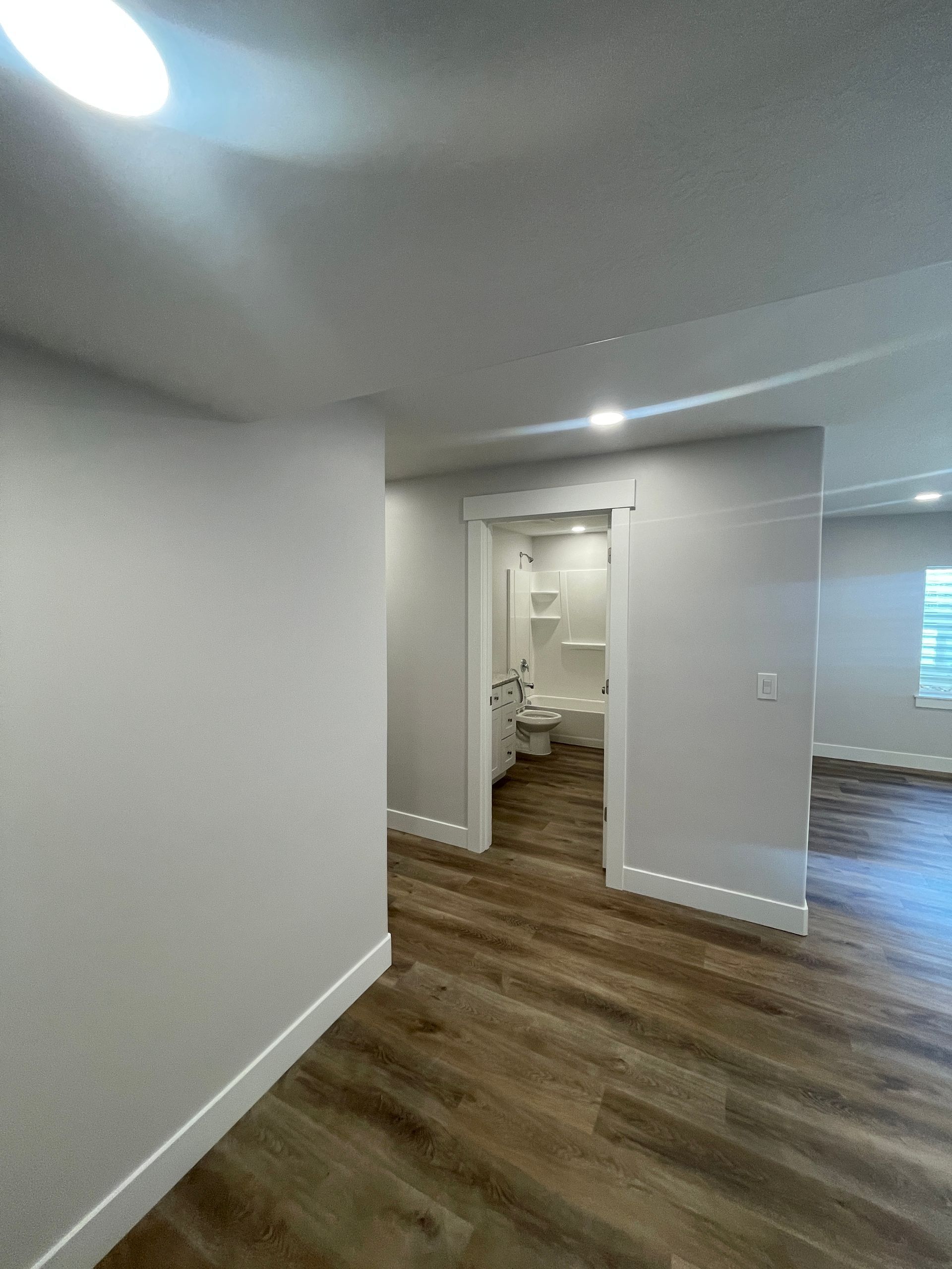 A hallway in a house with hardwood floors and white walls leading to a bathroom.