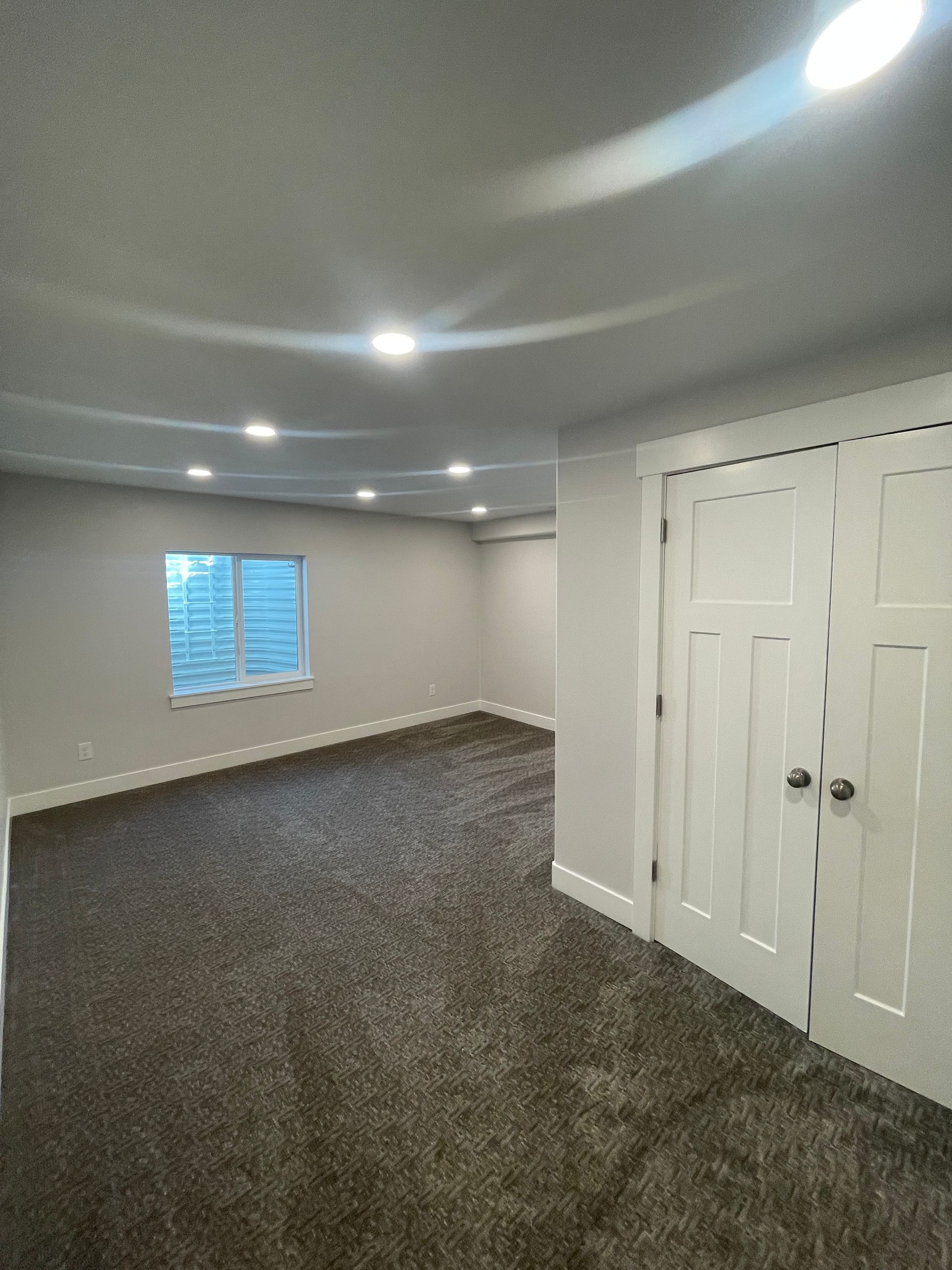 A large empty room with a carpeted floor and a window.