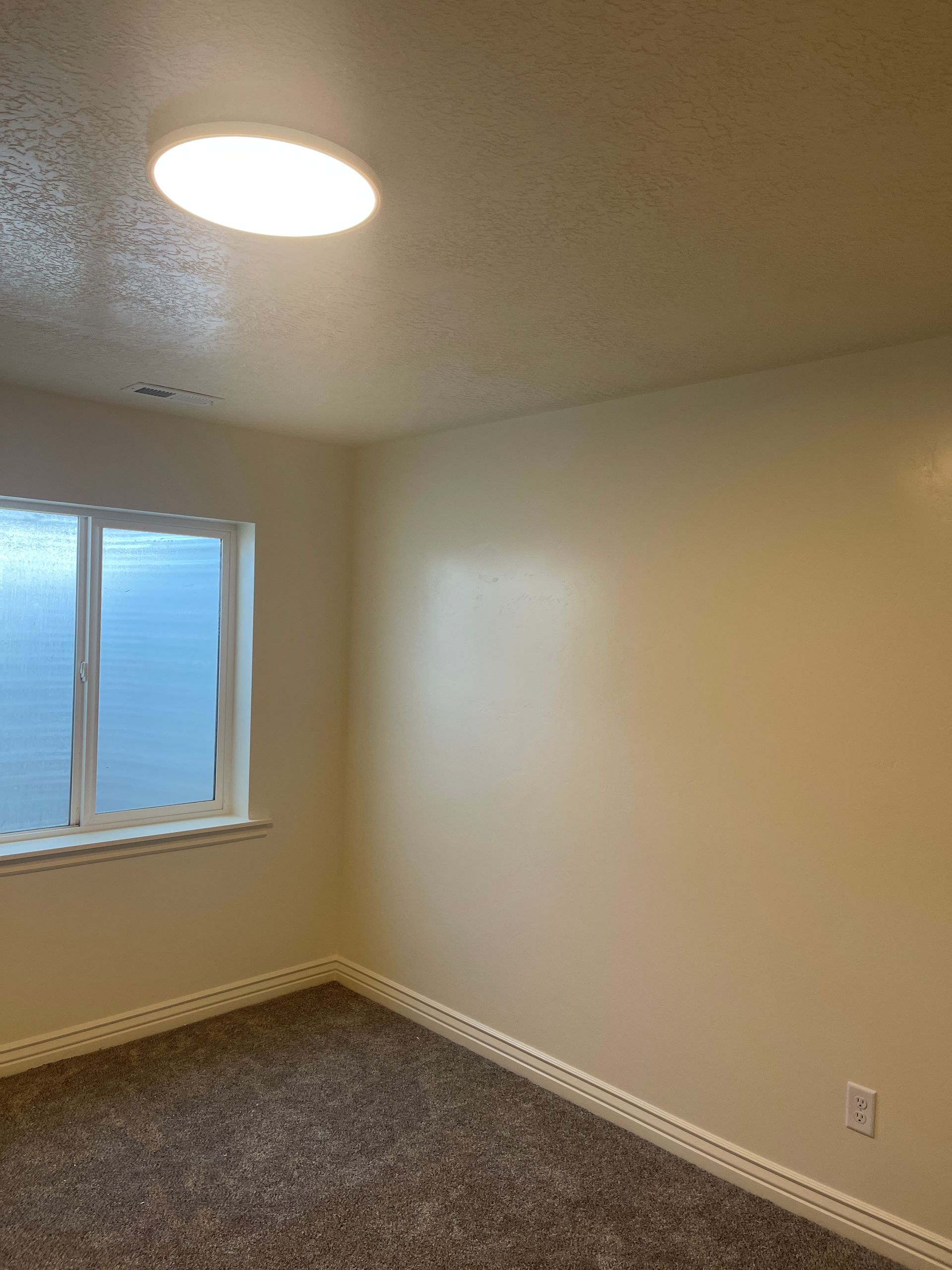 An empty bedroom with a window and a light on the ceiling.