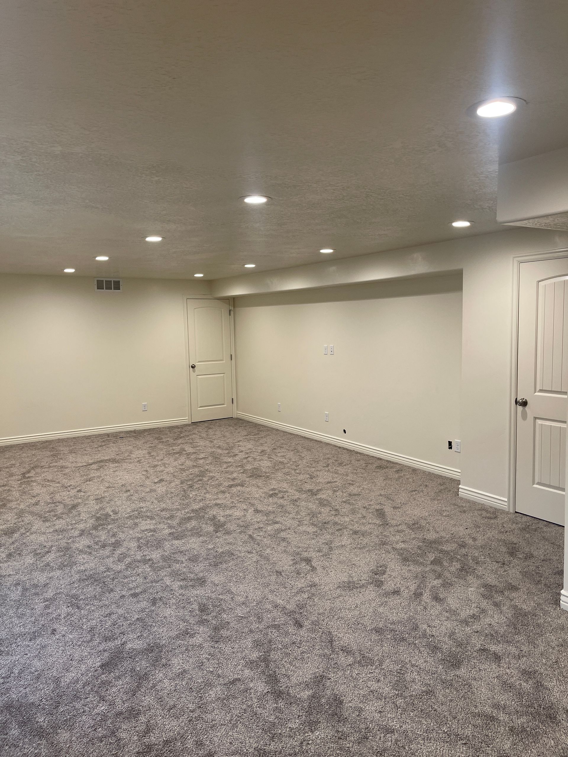 An empty basement with a carpeted floor and white walls.