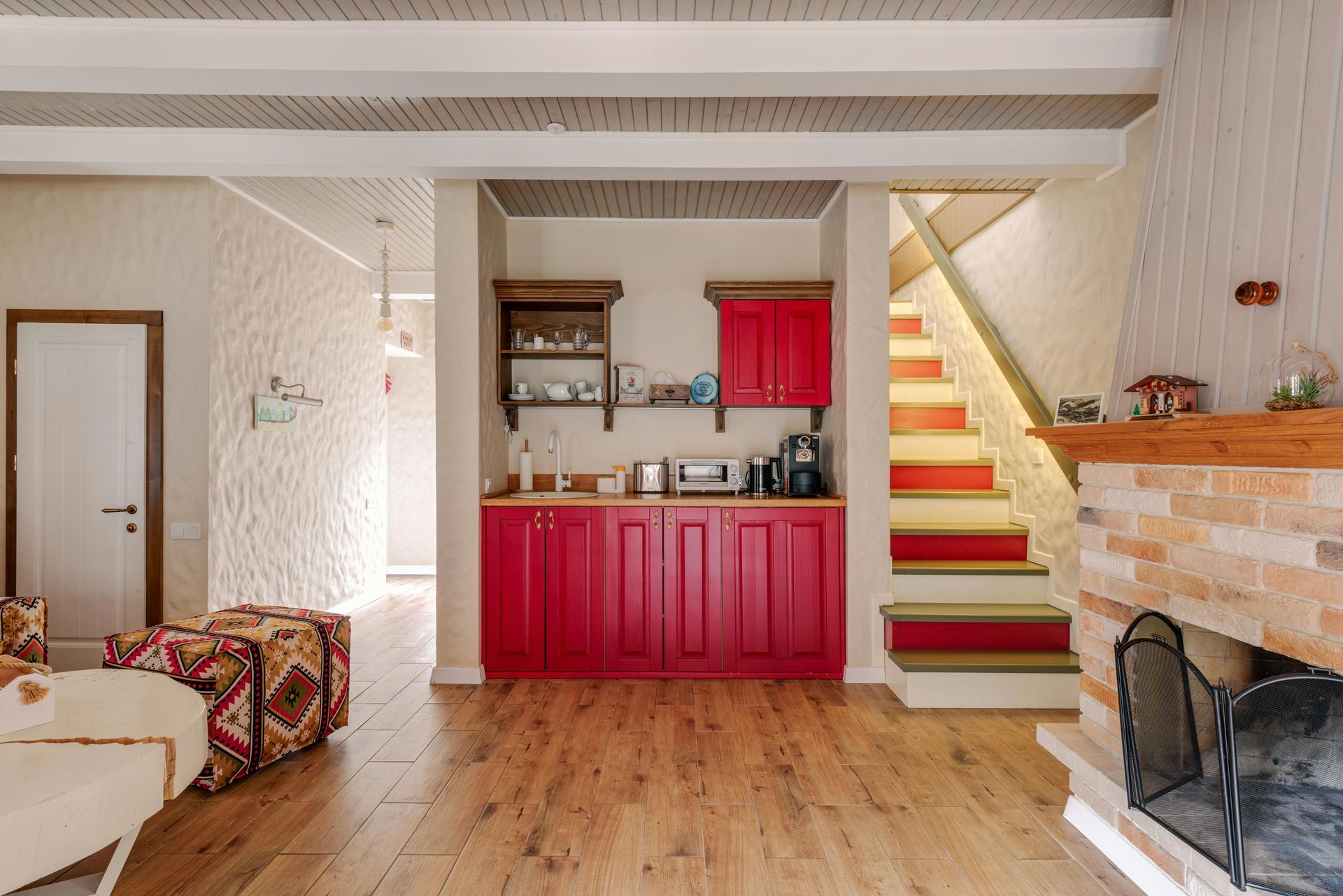 Basement kitchenette with red kitchen cabinets, staircase, and brick fireplace