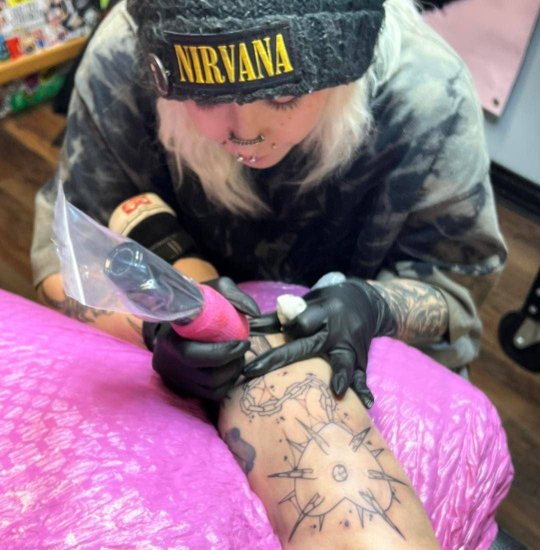 a woman wearing a nirvana hat is getting a tattoo on her arm