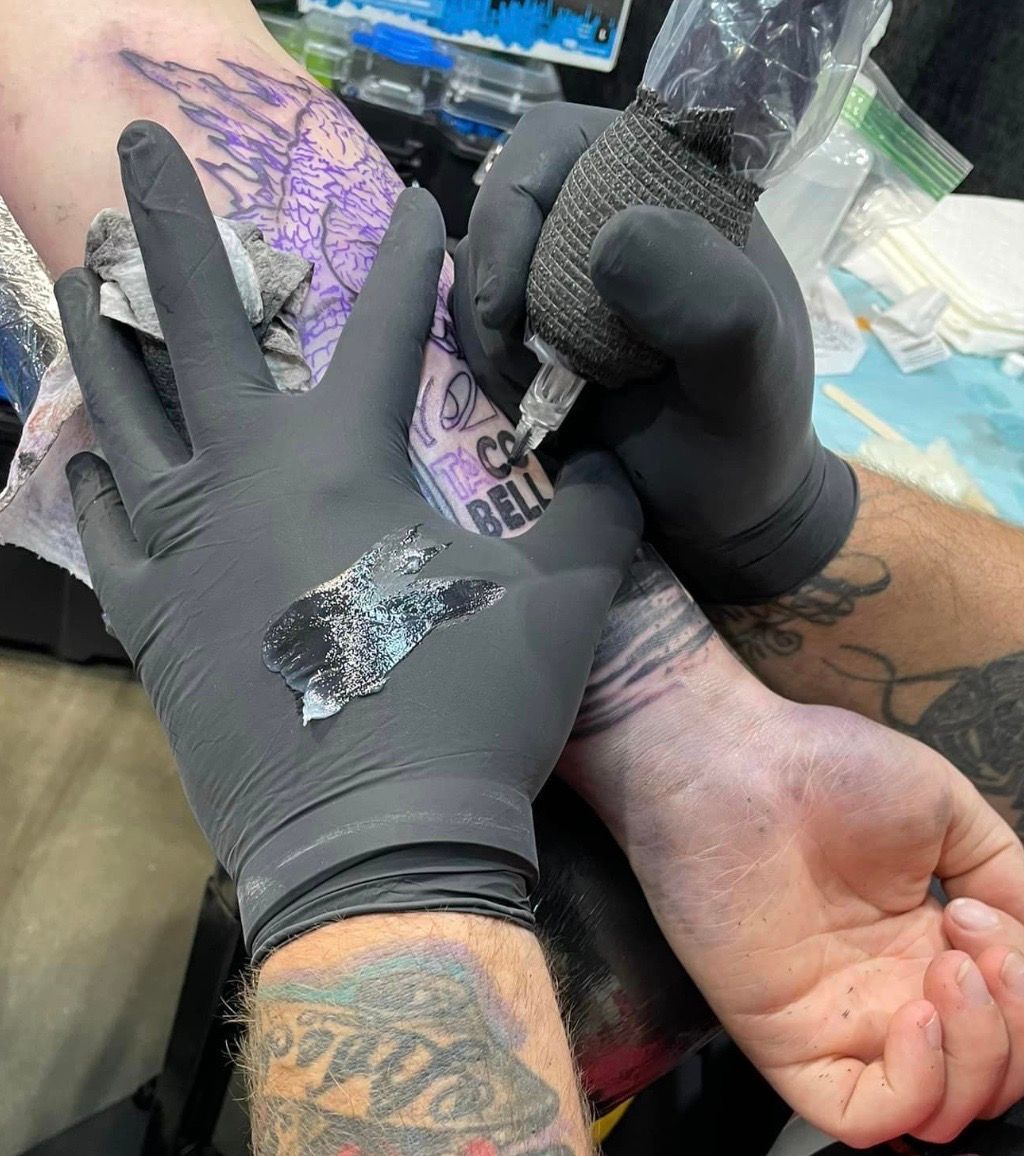 a person is getting a tattoo on their arm while wearing black gloves