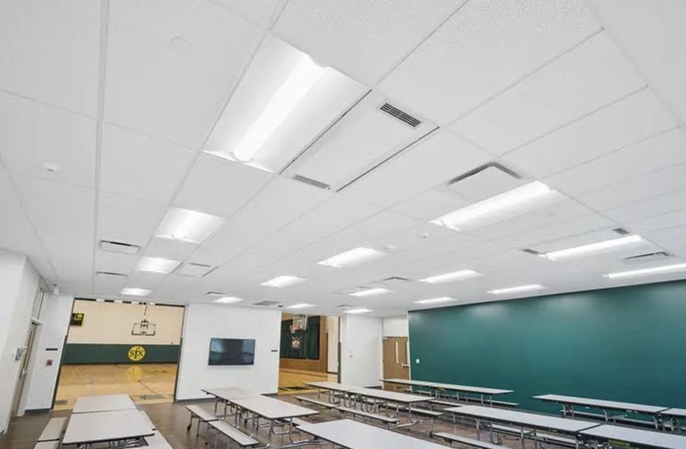 A large classroom with tables and benches and a basketball court in the background.