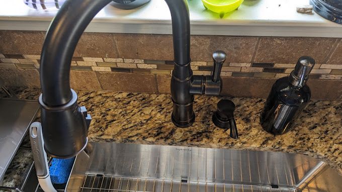 A kitchen sink with a black faucet and a soap dispenser on the counter.