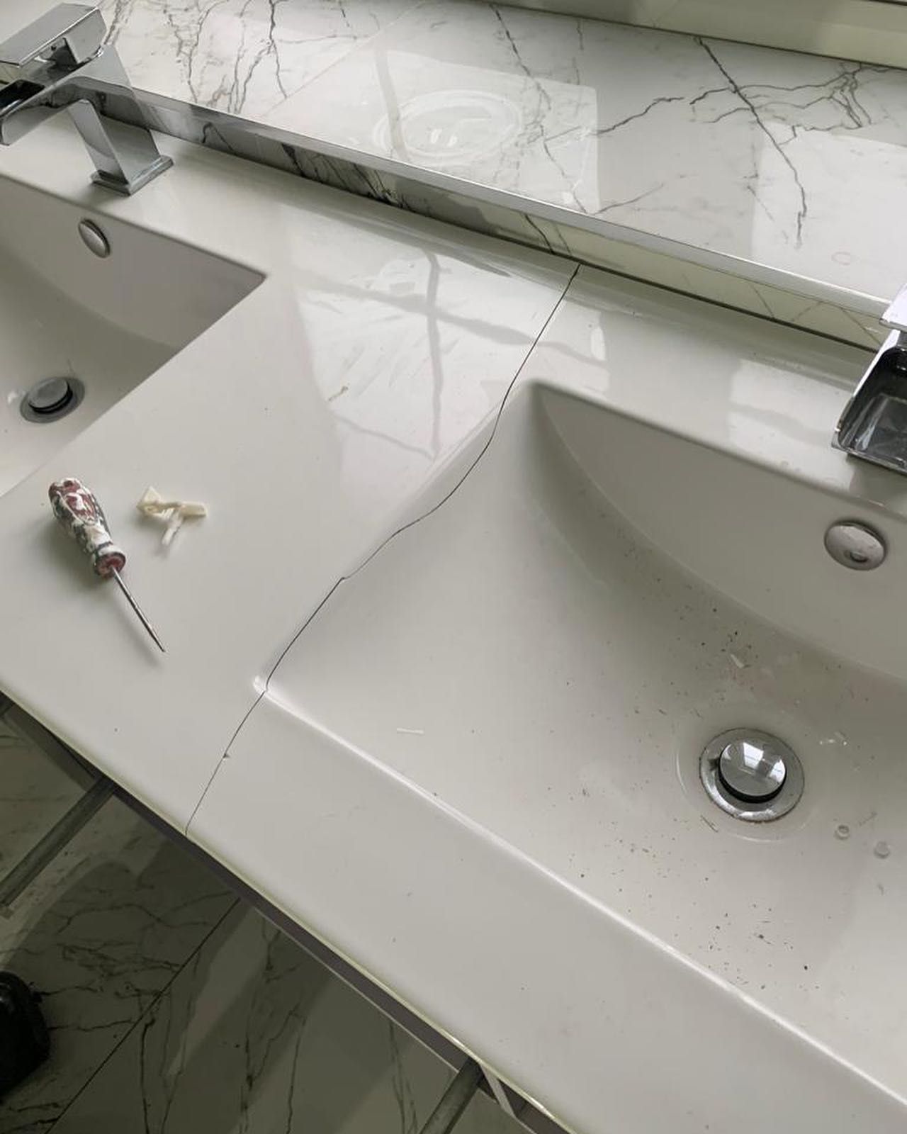 A bathroom sink with two sinks and a screwdriver on the counter.
