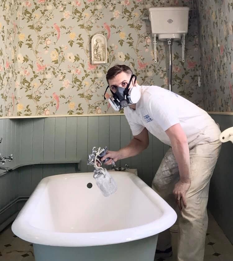 A man wearing a mask is spraying a bathtub in a bathroom