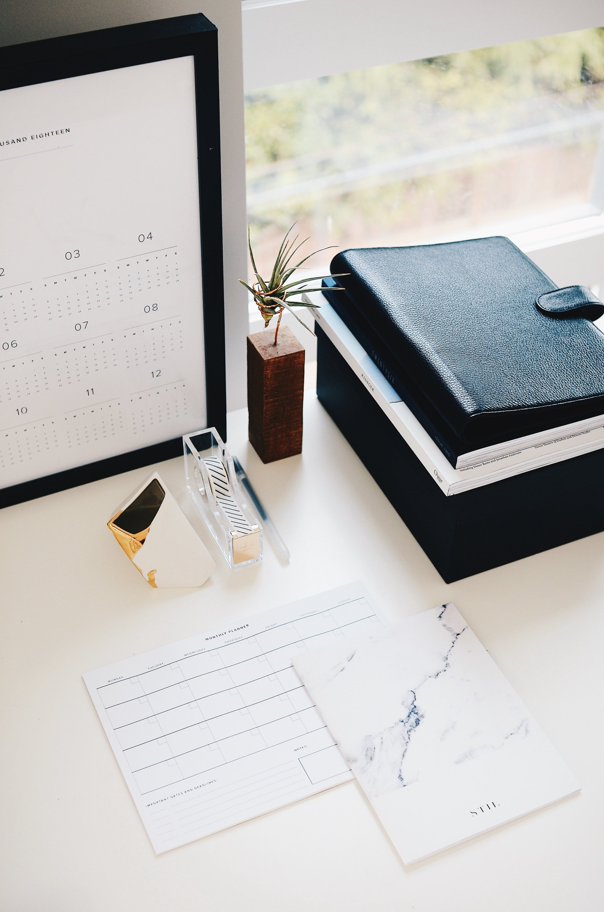 GK Marketing Online | A desk with a calendar , a notebook , a pen , and a vase of flowers.