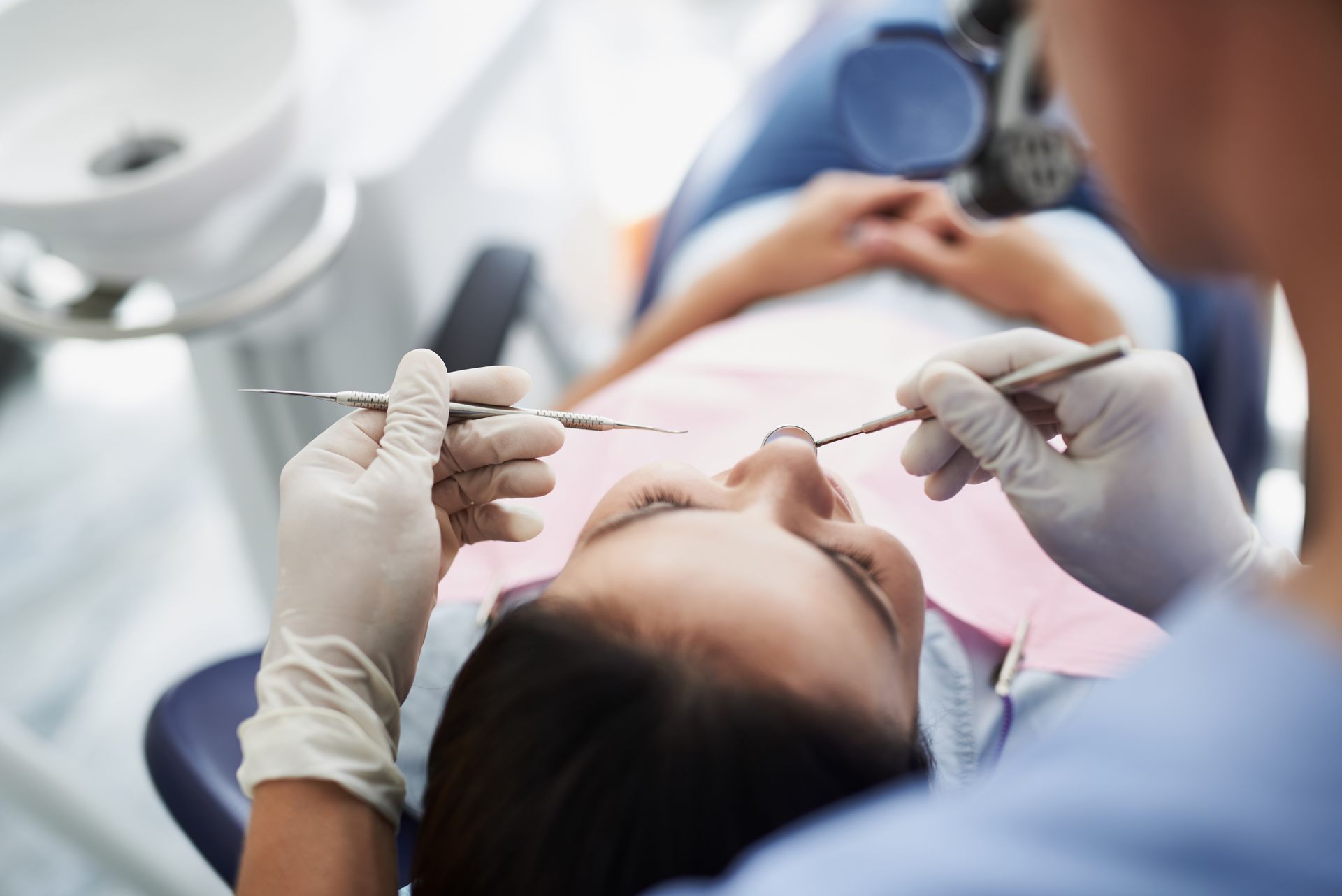 A woman is laying in a dental chair getting her teeth examined by a dentist.