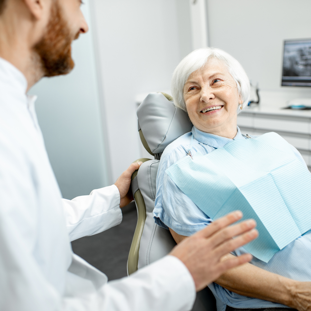 An elderly woman is sitting in a dental chair talking to a dentist.