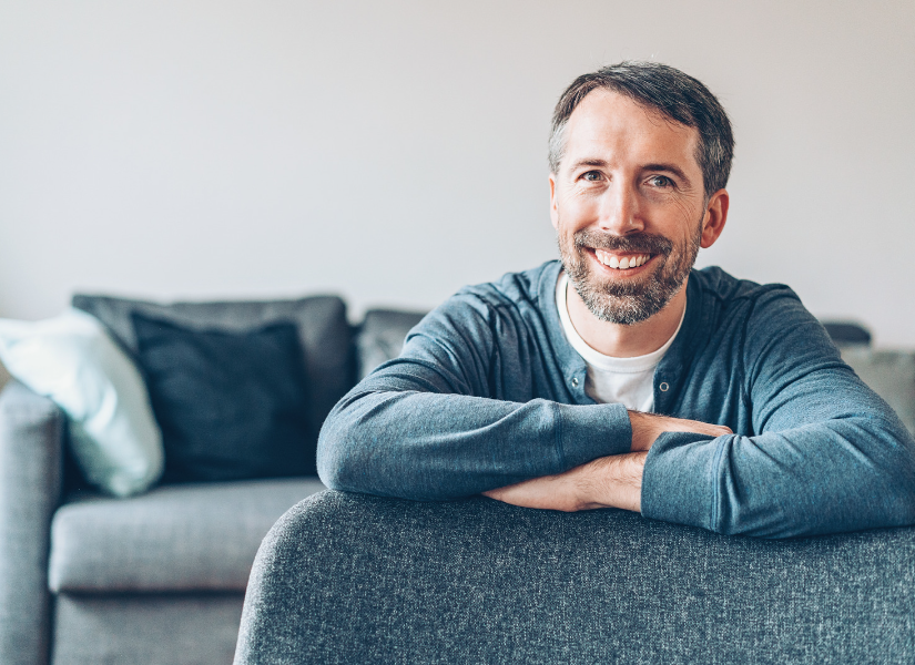 A man is sitting on a couch with his arms crossed and smiling.