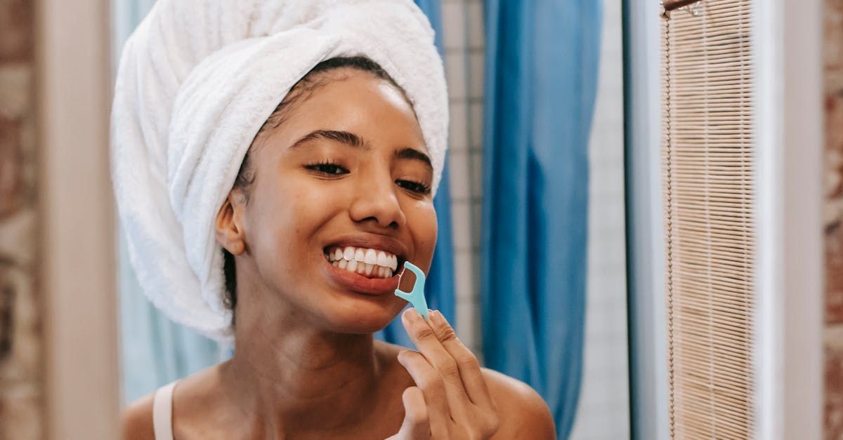 A woman with a towel wrapped around her head is brushing her teeth in front of a mirror.