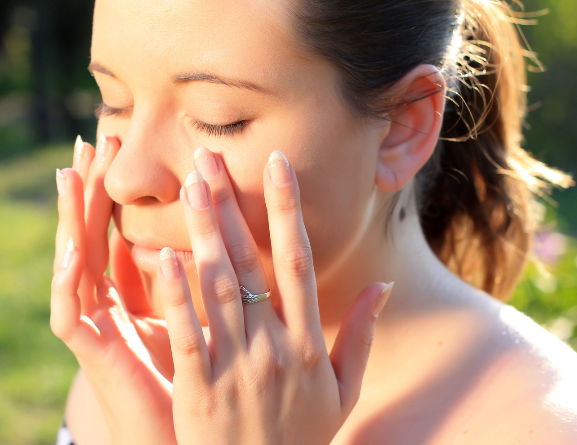 A woman with a ring on her finger is applying sunscreen to her face