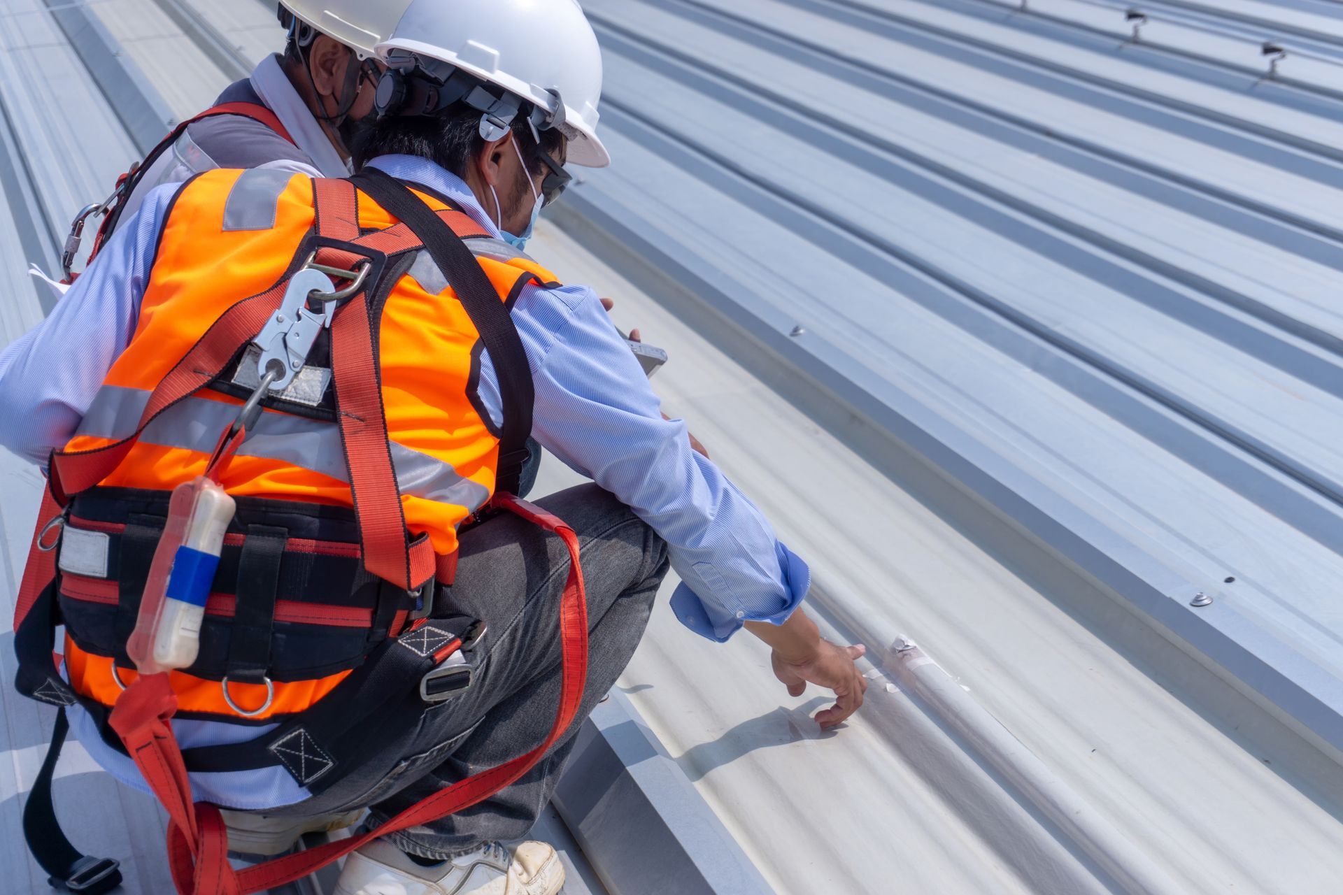 Des ouvriers portant des harnais de sécurité haute visibilité et des casques de chantier inspectent l'installation d'une toiture métallique.