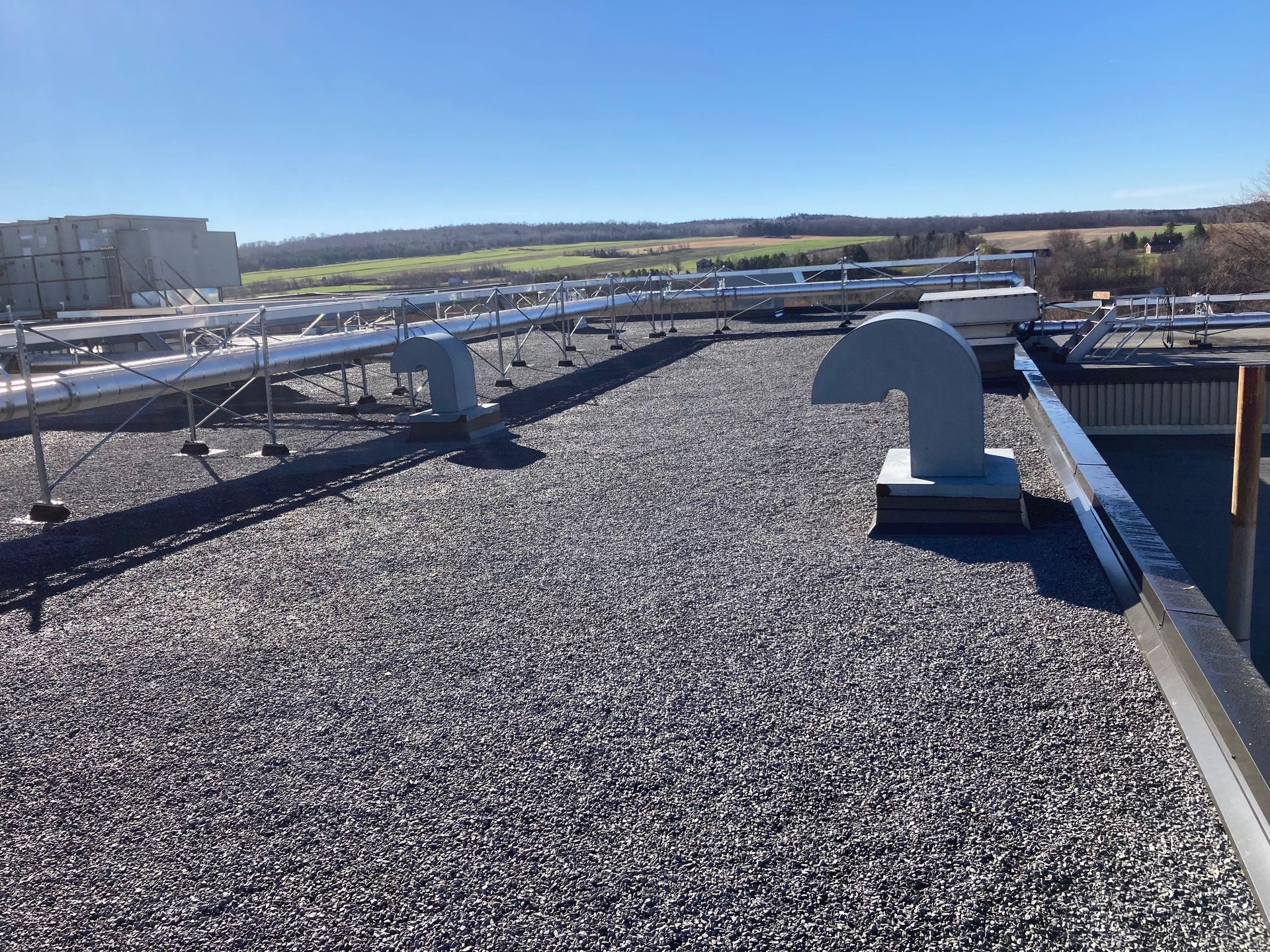 Le toit d'un bâtiment commercial recouvert de gravier, sous un ciel bleu, avec des conduits de ventilation mécanique et une charpente métallique.