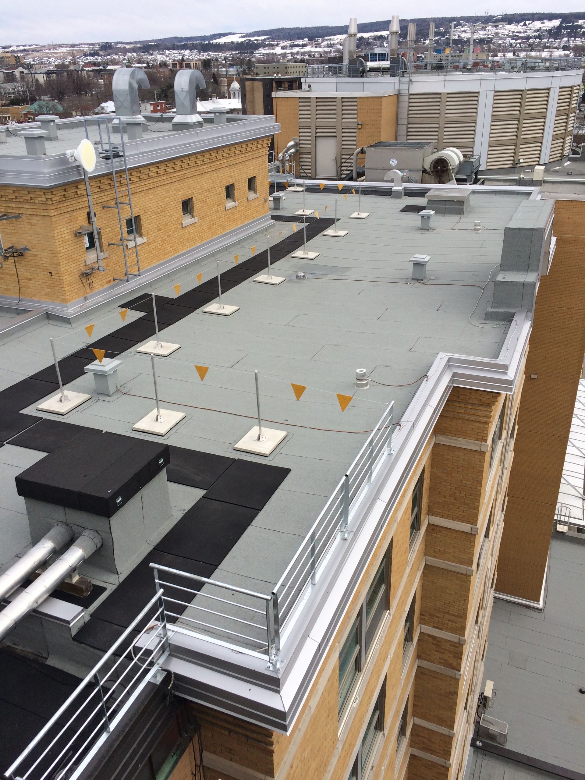 Vue aérienne d'un toit plat commercial avec unités de climatisation, bouches d'aération, garde-corps métalliques et lignes de signalisation jaunes.