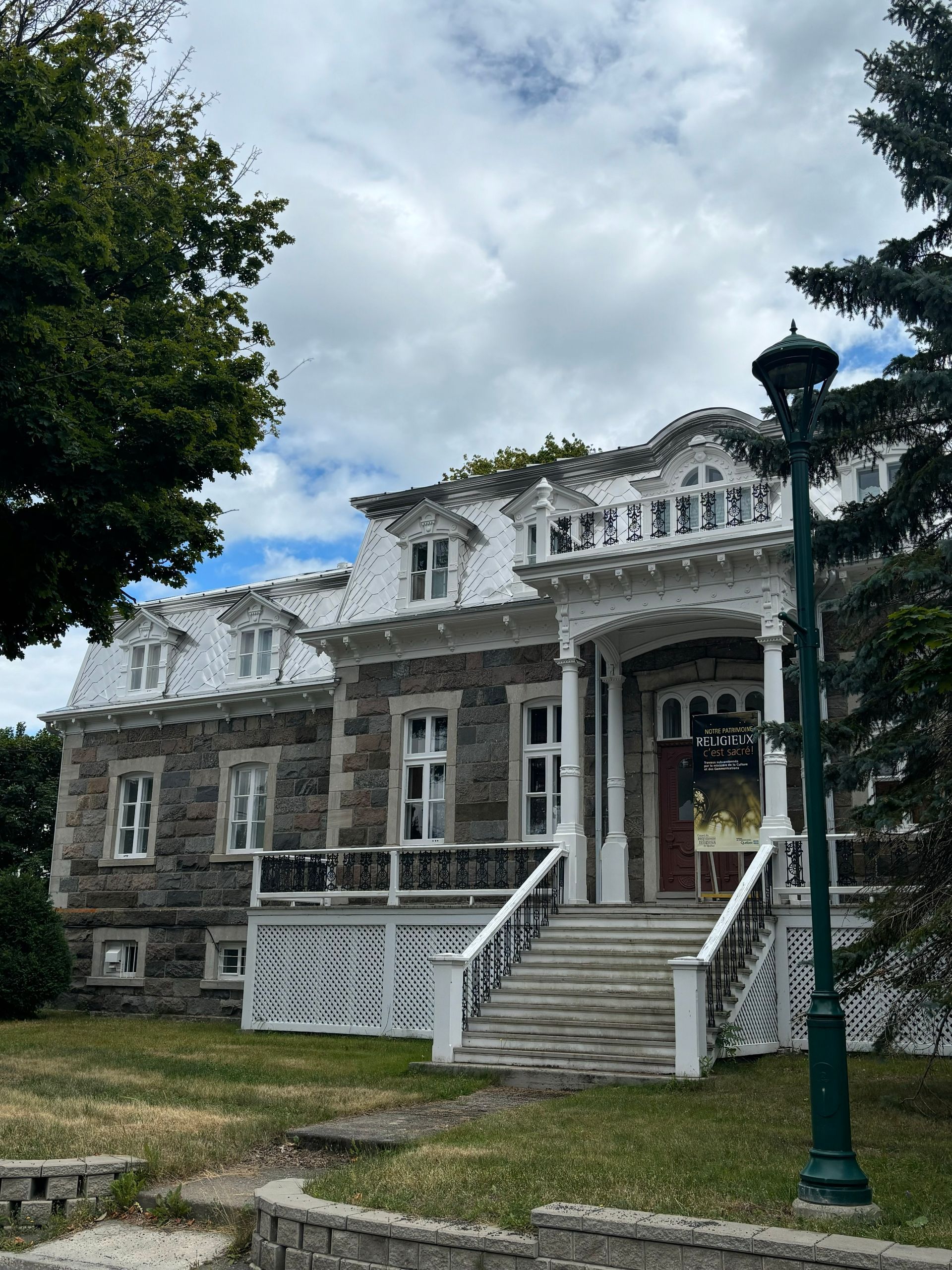 Un bâtiment en pierre aux ornements blancs, un toit pentu, des lucarnes et un escalier menant à une entrée principale.