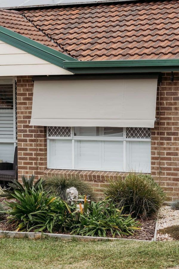 A Brick House with A White Awning on The Window — New Blinds and Shutters in Maryland, NSW