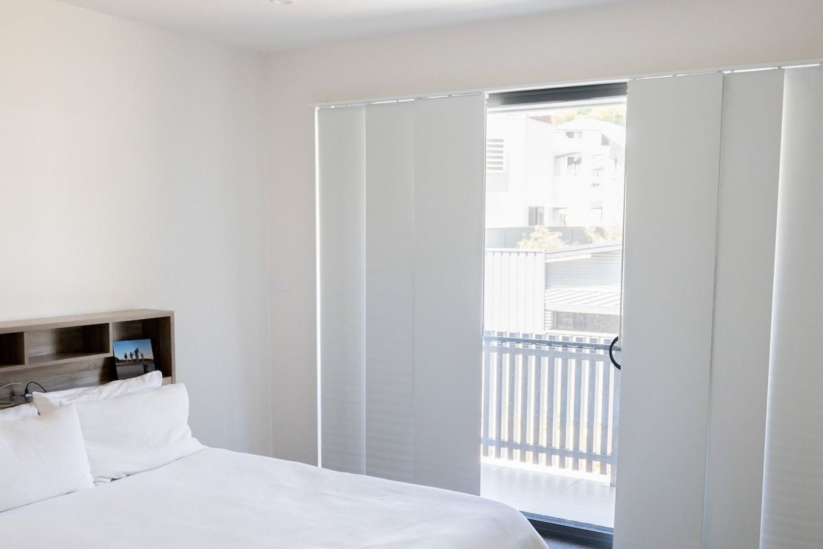 A Bedroom with A Bed and A Sliding Glass Door Leading to A Balcony — New Blinds and Shutters in Maryland, NSW