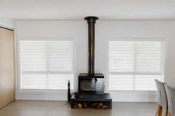A Wood Stove Is Sitting in A Living Room Next to Two Windows — New Blinds and Shutters in Maryland, NSW