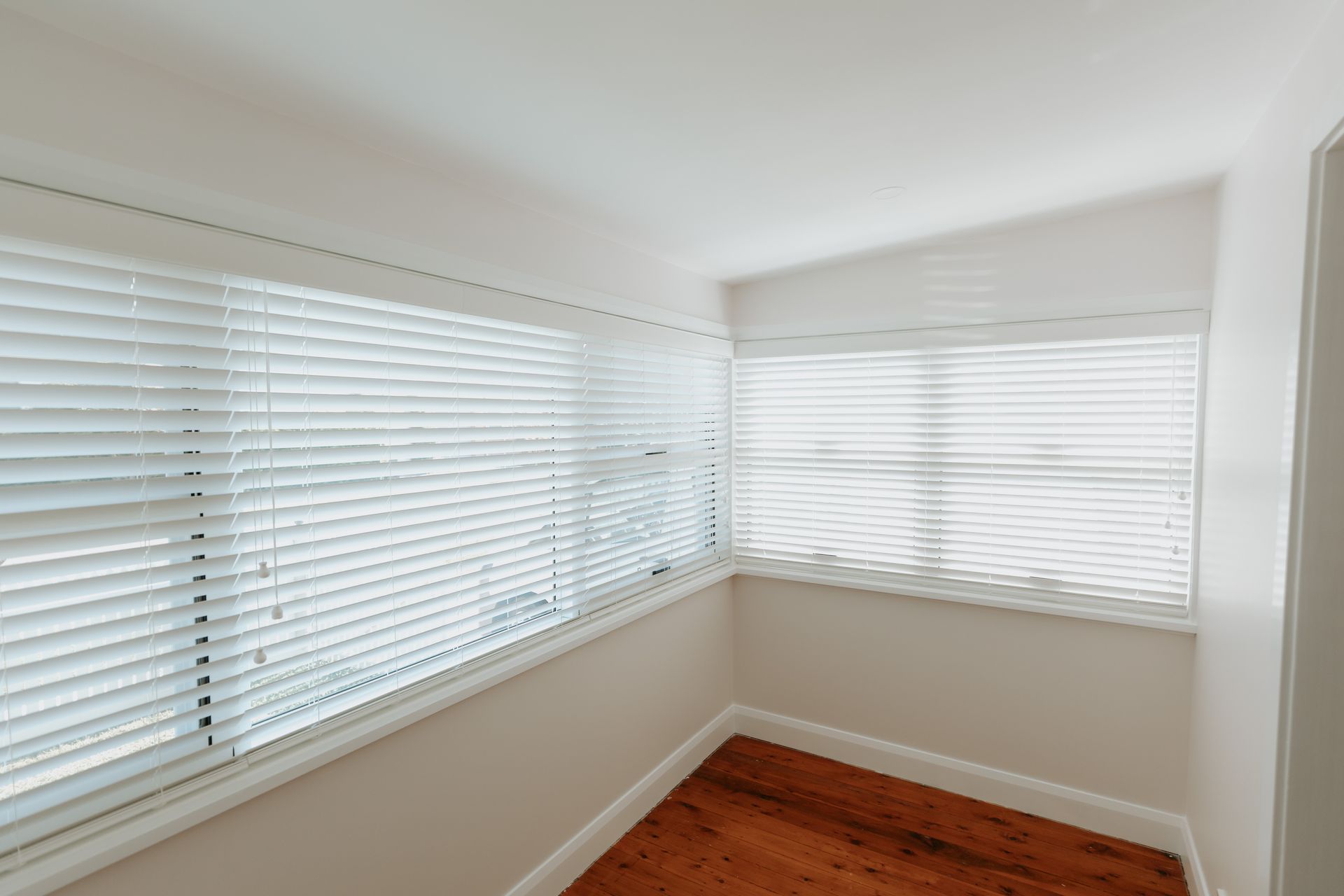 An Empty Room with Wooden Floors and White Blinds on The Windows — New Blinds and Shutters in Maryland, NSW