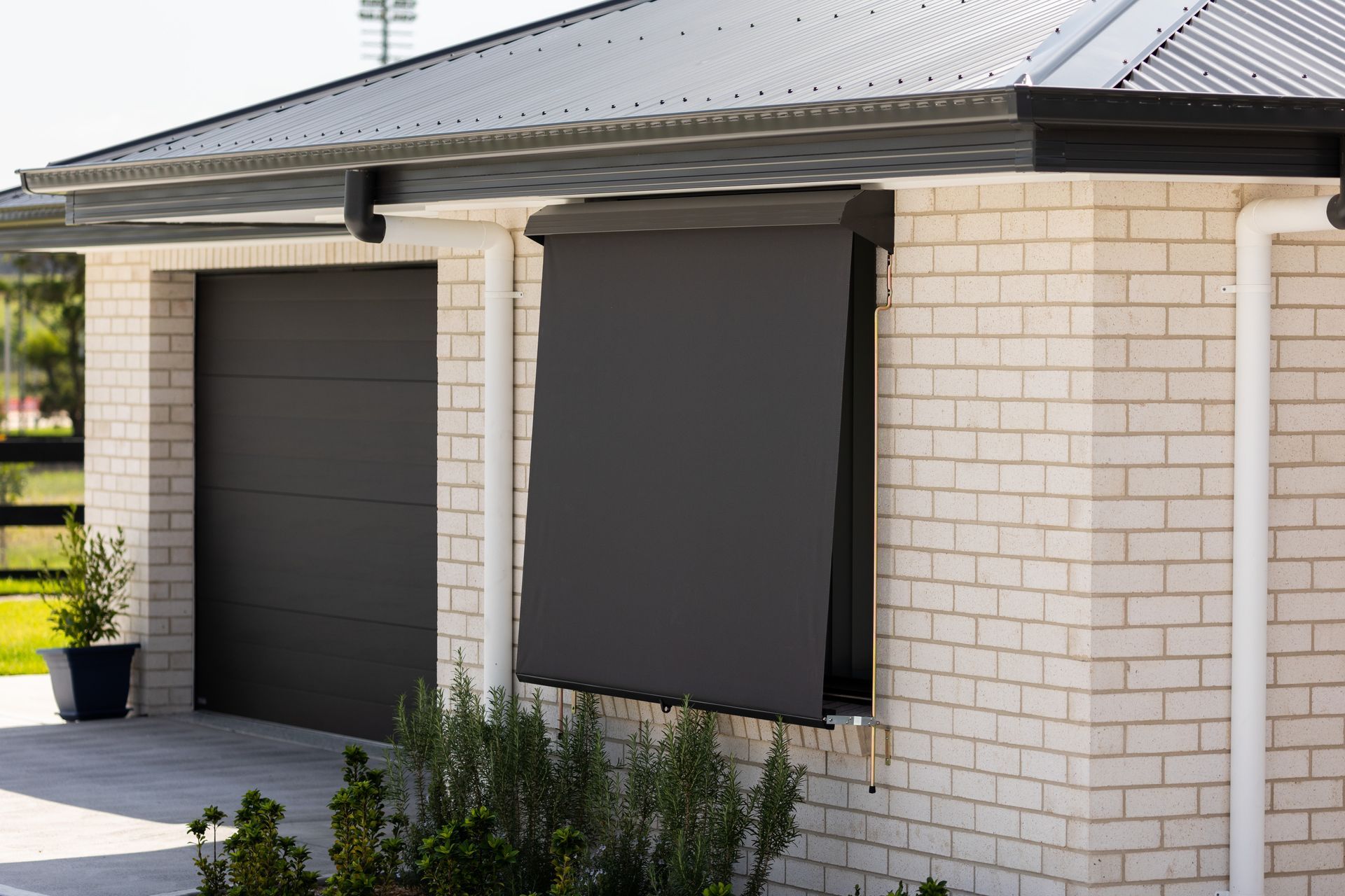 A White Brick House with A Black Garage Door and A Black Awning on The Window — New Blinds and Shutters in Charlestown, NSW