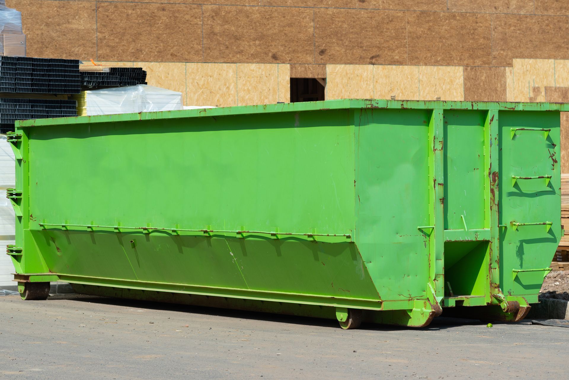 Green dumpster on wheels, outdoors, near building construction. Green dumpster on wheels, outdoors, near building construction.