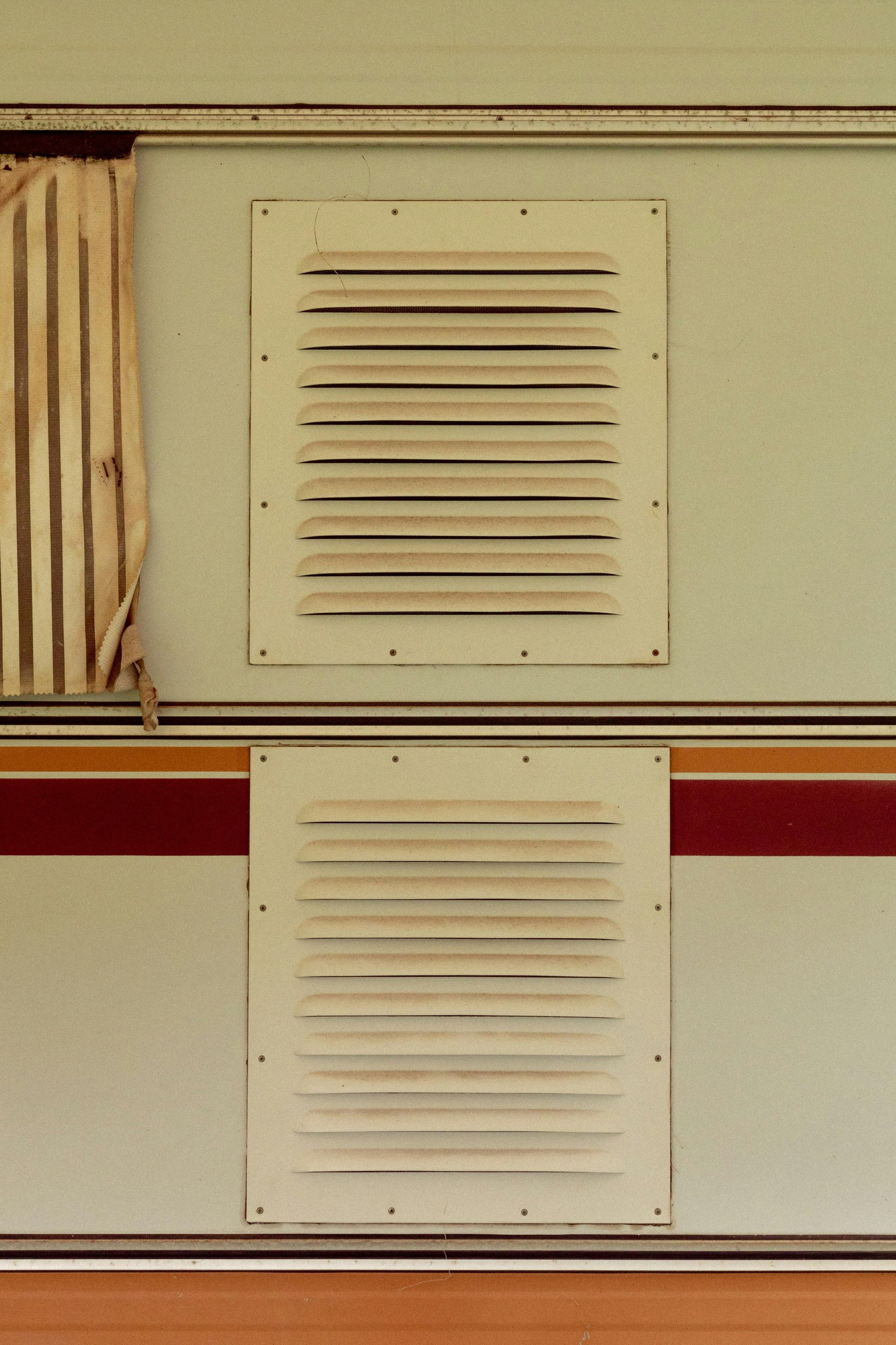 White and beige RV exterior with two rectangular vents, brown and red stripe, and a curtain.